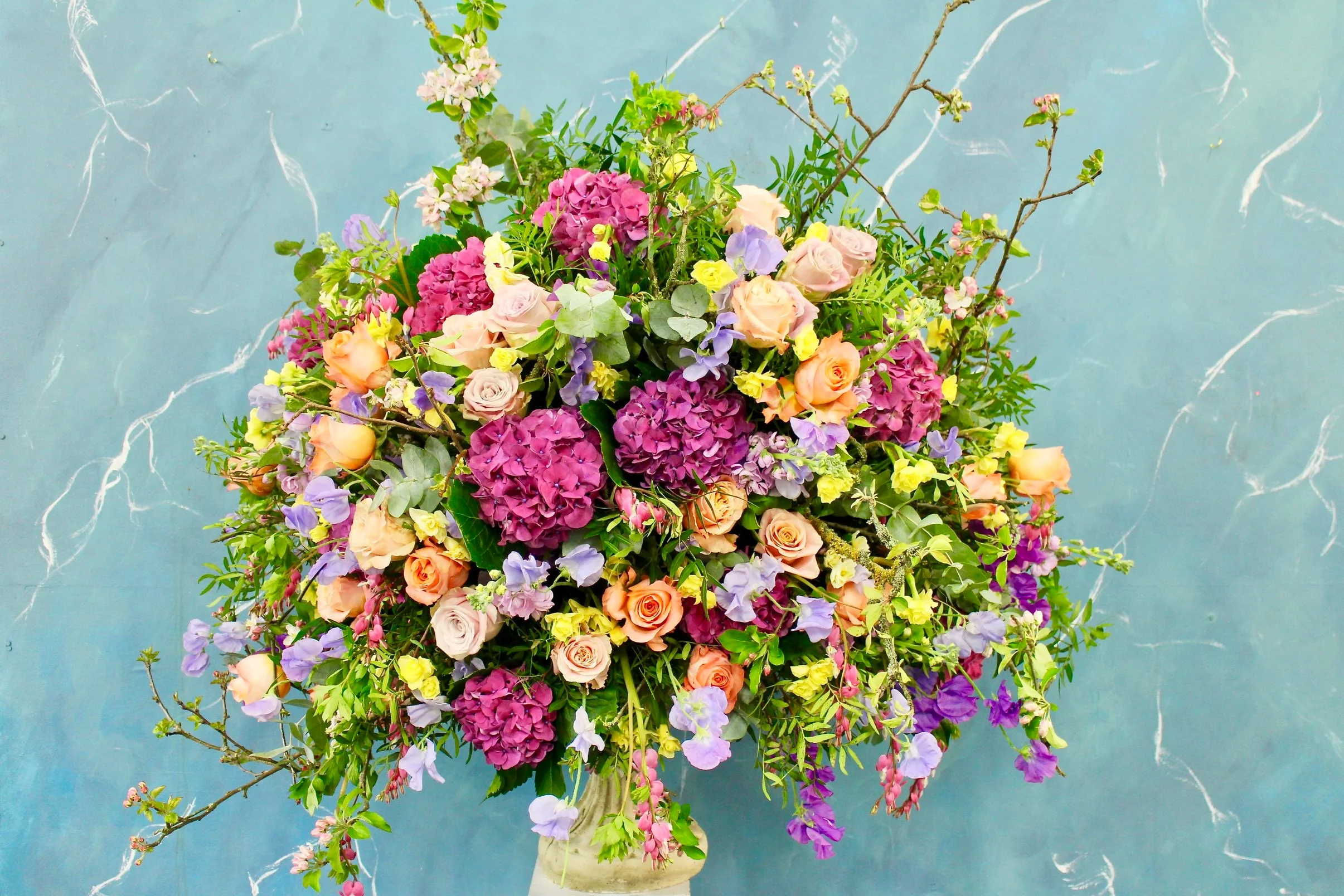 A spring urn filled with hydrangea, faith roses, apple blossom, sweet peas, daffodils, and an abundance of textured foliage