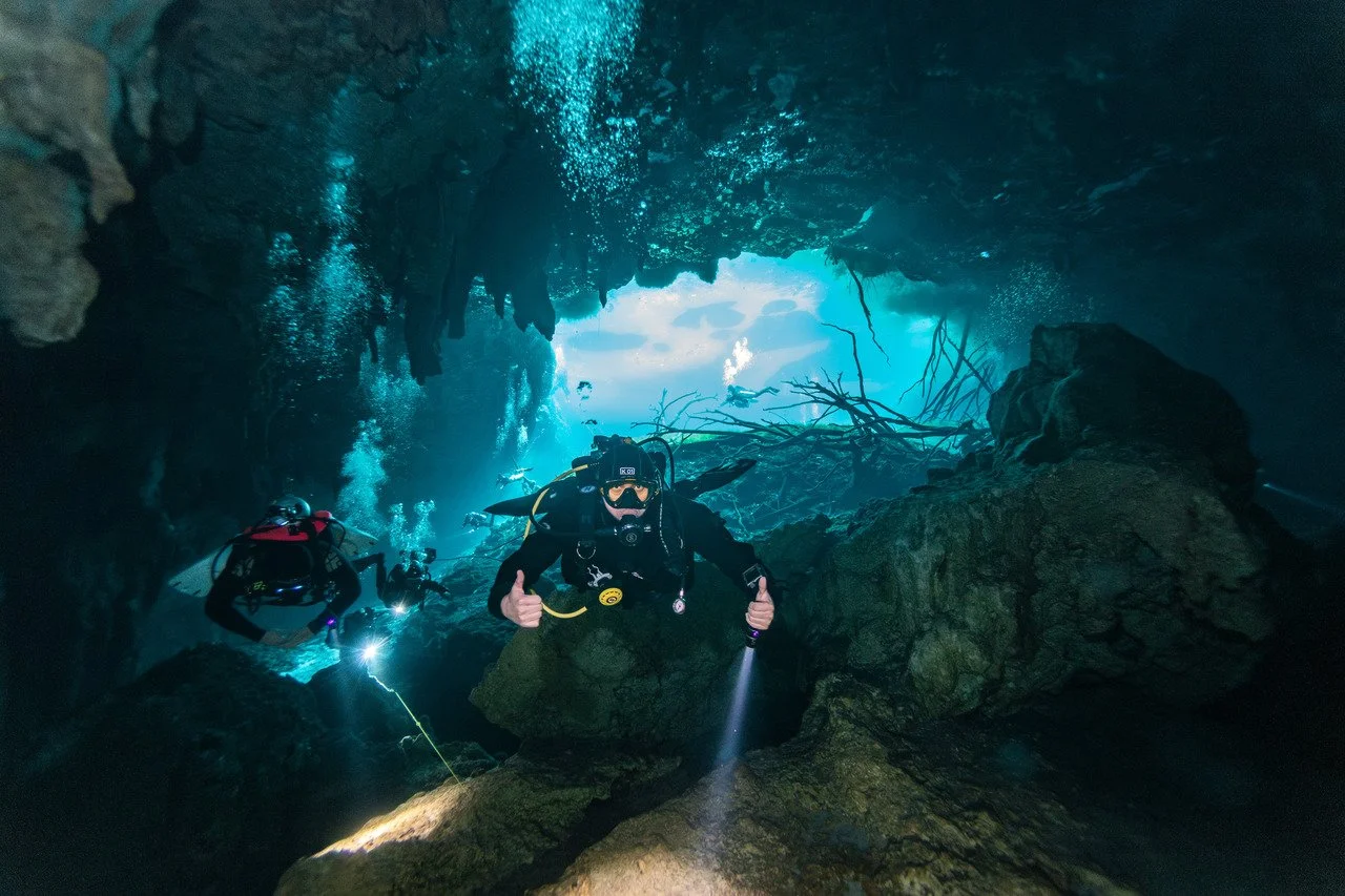 scuba divers entering the darker cavern section of car wash cenote contrasted with the bright blue of the open section
