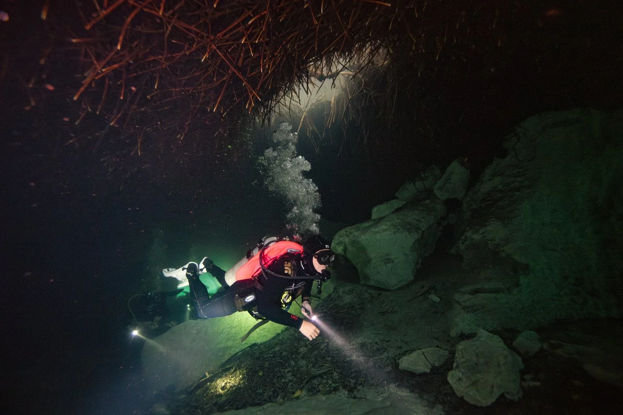 A scuba diver exploring an underwater cave with a flashlight.