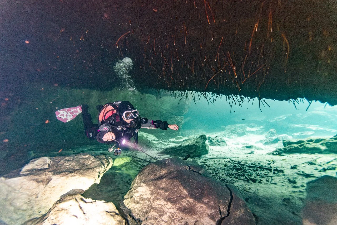 Diver in a swim through at casa cenote with sunlight shining in the distance