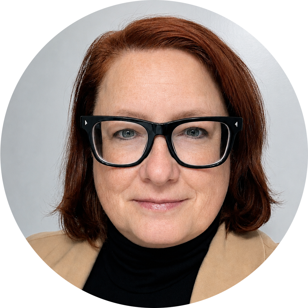 Woman facing forward with a slight smile. Light skin, reddish-brown hair and black glasses. Wearing a black turtleneck sweater and a camel colored jacket.