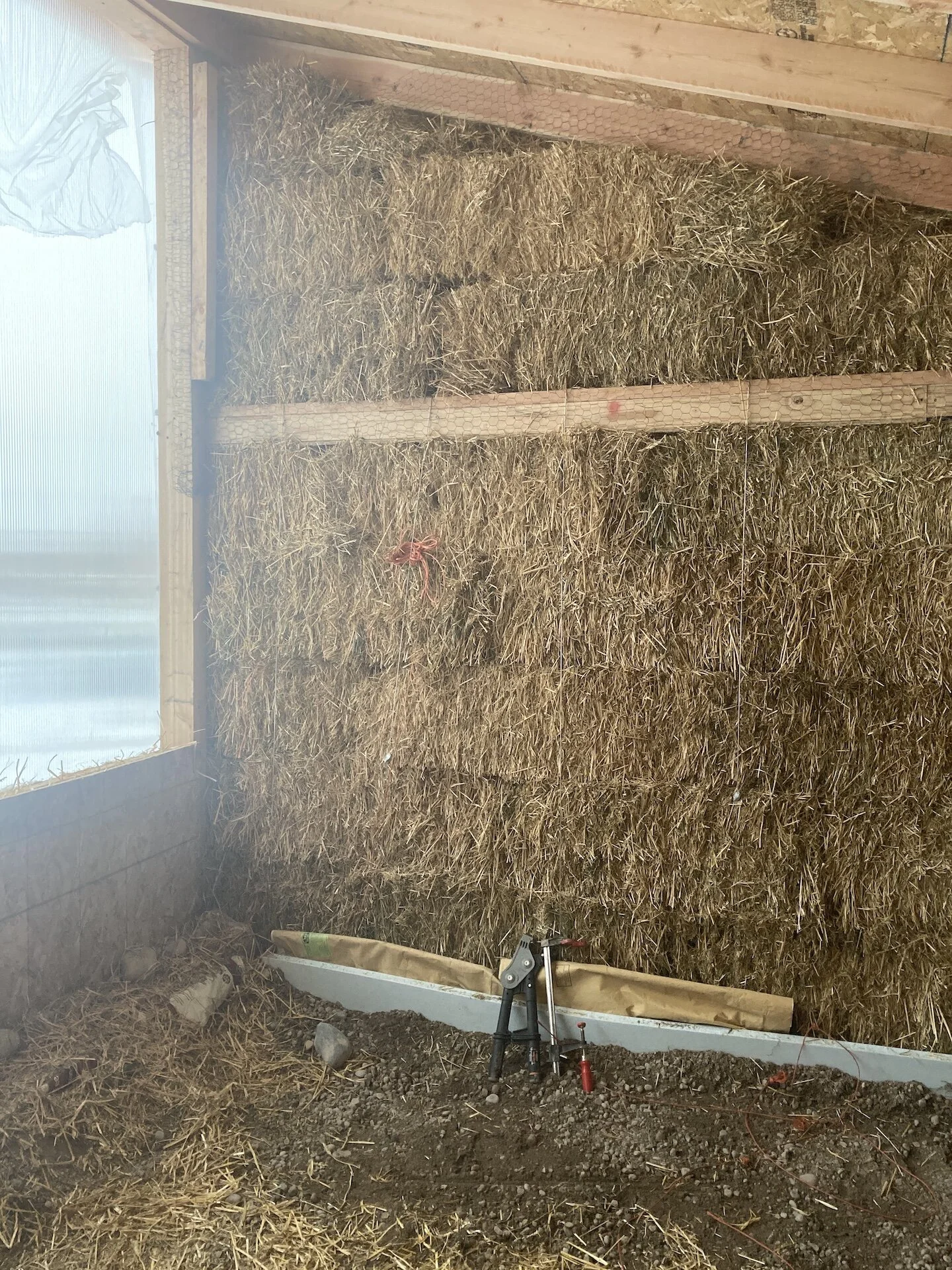  The base of the walls, where the bales meet the gabions were blocked with some scrap blue board pieces around the inside perimeter.  Until we had everything mudded, feed bags were used to block drafts.  Feed bags were also used below the windows to 