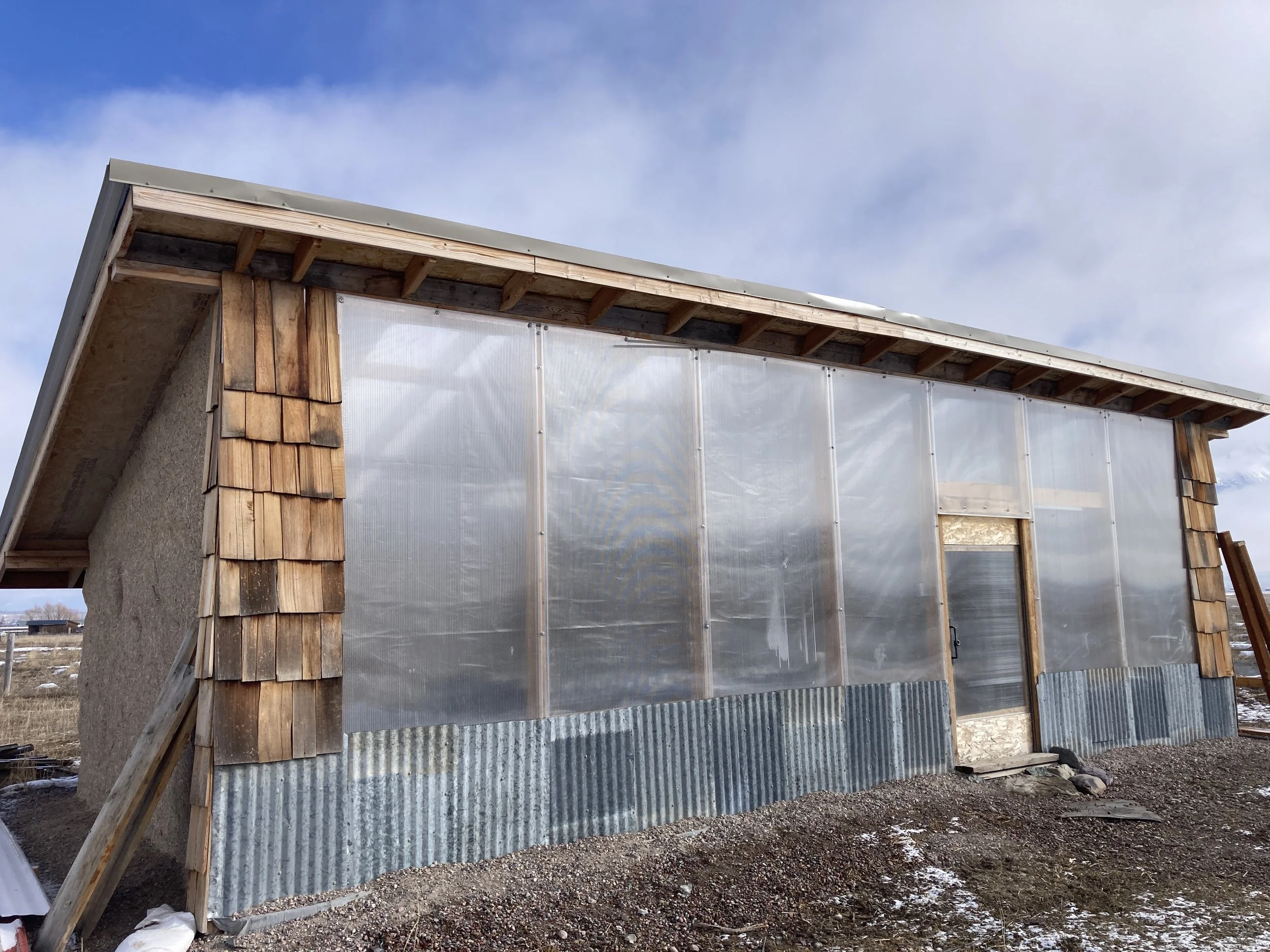  Mostly finished south wall.   Skylights and interior greenhouse plastic are installed.  Scavenged cedar shingles and corrugated steel sheeting were used as siding.   