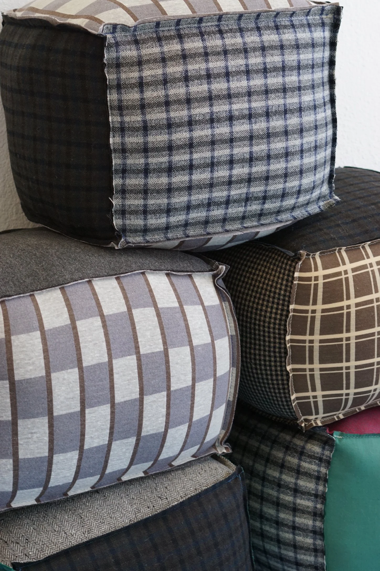 Stack of six fabric-covered cushions with various plaid and checkered patterns in shades of brown, blue, black, and gray.