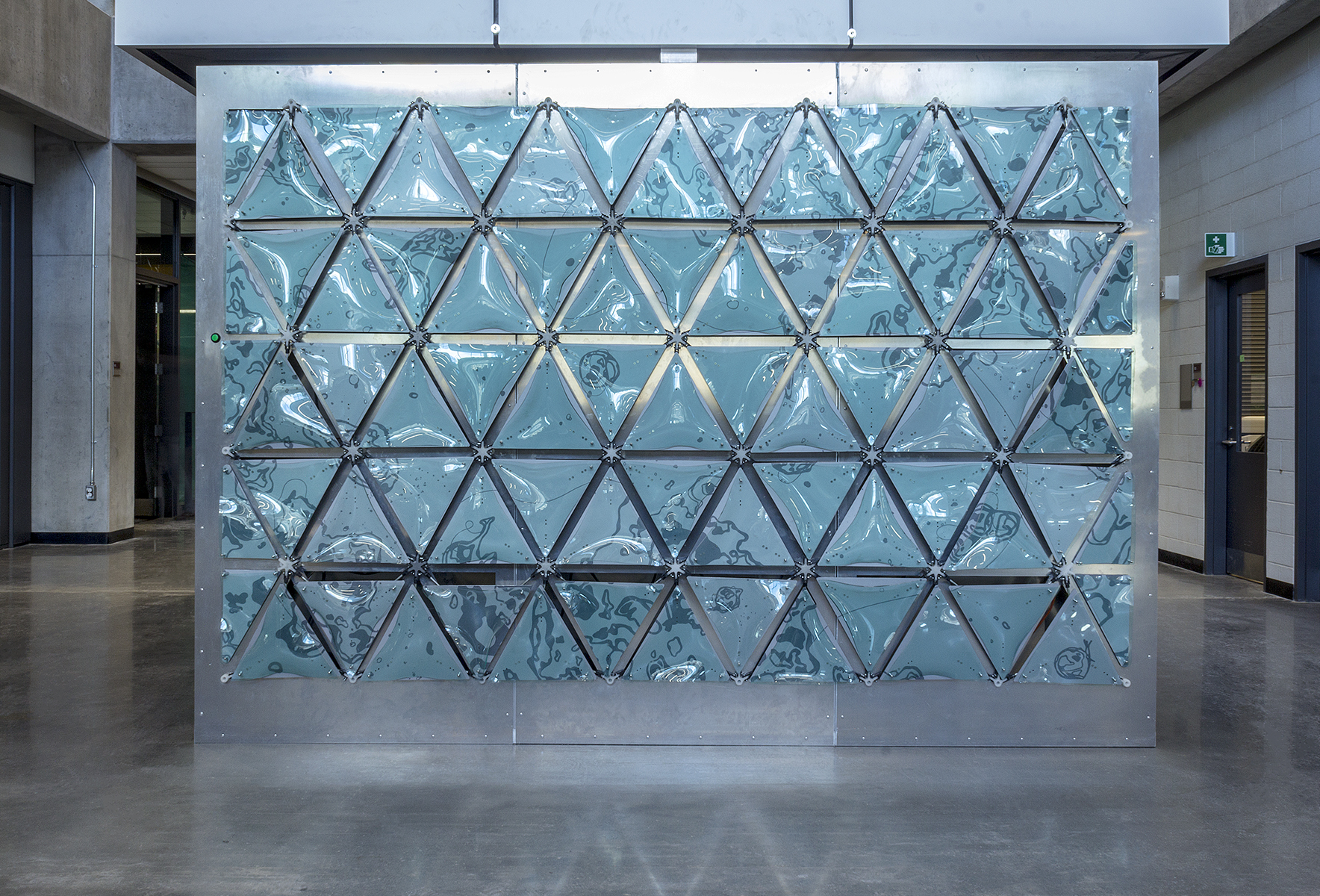 Surface Tension, Mixed Media (2018) Keshav Deeljur, Sarah Hodgson, Lucy Oulanova, Devansh Shah This is an interactive artwork produced through the collaboration of artists and engineers. It resides in the STEM Complex at the University of Ottawa. Surface tension describes the force of attraction between individual water molecules creating a bond resistant to external pressure. This phenomenon is a beautiful display of strength, cooperation, and unity. The team was inspired by this phenomenon and drew inspiration from it visually and metaphorically. The team began their research by taking water samples from the Ottawa River. They then documented their findings through microscopic photographs. The photographic research translated into the line drawings that are scrolled across the paneled wall. The drawings are microorganisms, as well as other biotic factors. The panels are interconnected and smoothly programmed to create an undulating motion reminiscent of water. This metaphor of water is aided by the raised acrylic which simulates the play of light over the surface of water. This project was made possible with the generous support of the Engineering Faculty and Visual Arts Department of the University of Ottawa Special thanks to: Hanan Anis, Chris Falconi, Atticus Gordon, David McDougall, Sarmad Nomani, Nikhil Peri, Sasha Phipps, Chantal Rodier, Laura Weller, Ali Sanaknaki, and Mohamed Abdrabou