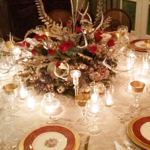 Elegant Christmas dinner table with gold antler centerpiece, red roses, candles, gold-rimmed china plates, and crystal glassware