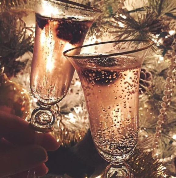 Two glasses of sparkling rosé champagne with berries clinking in a festive holiday celebration with warm lights in the background.