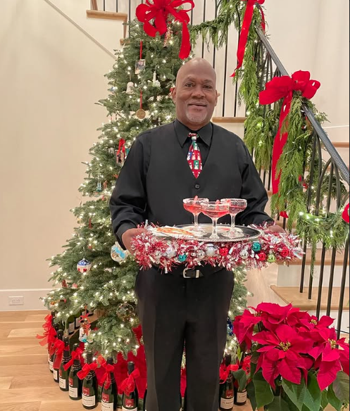 Professional catering server in formal attire providing festive cocktail service in front of an elegant Christmas tree, ideal for holiday events and private catering.