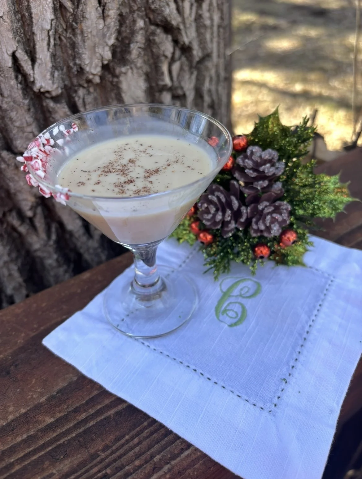 Creamy eggnog martini with crushed candy cane rim and nutmeg garnish on white linen napkin with festive pine cone decoration