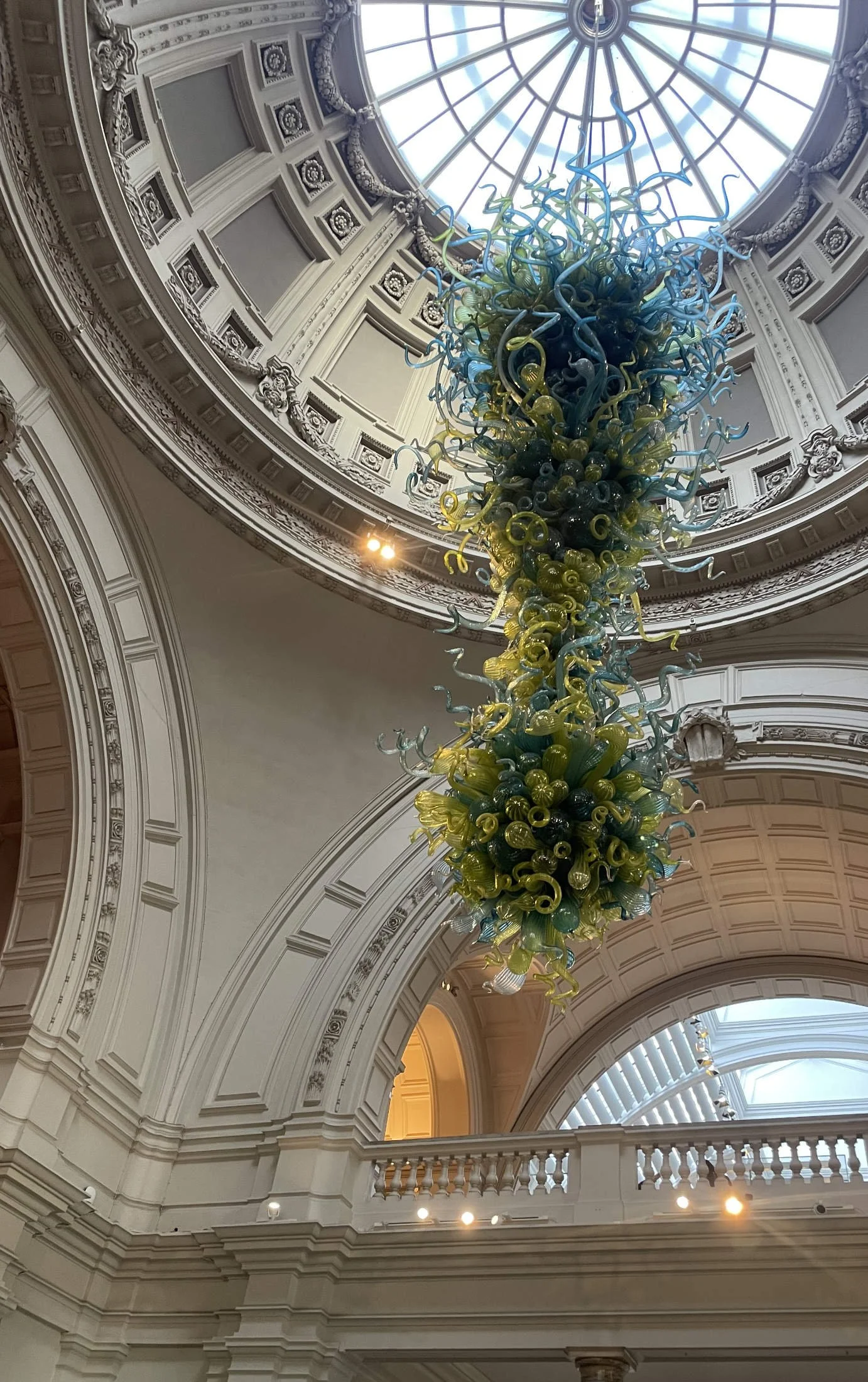  Blue and green Chihuly glass chandelier suspended under a grand domed skylight inside the Victoria and Albert Museum, London. 