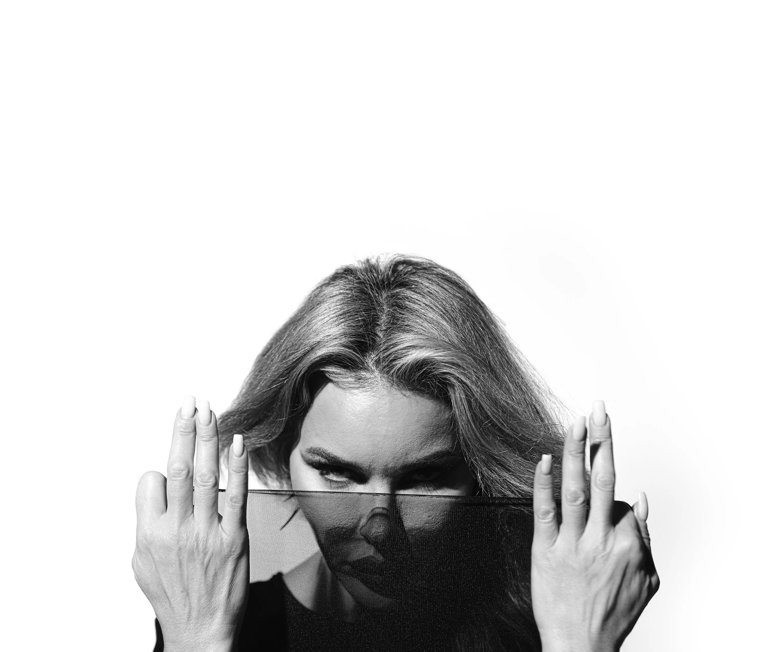 Close-up black and white portrait of a person peering over a sheer black fabric veil with an intense gaze by Metty Unuabona
