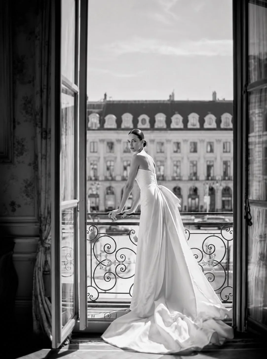 Elegant bride in a couture wedding gown overlooking Place Vendôme from a Parisian balcony.