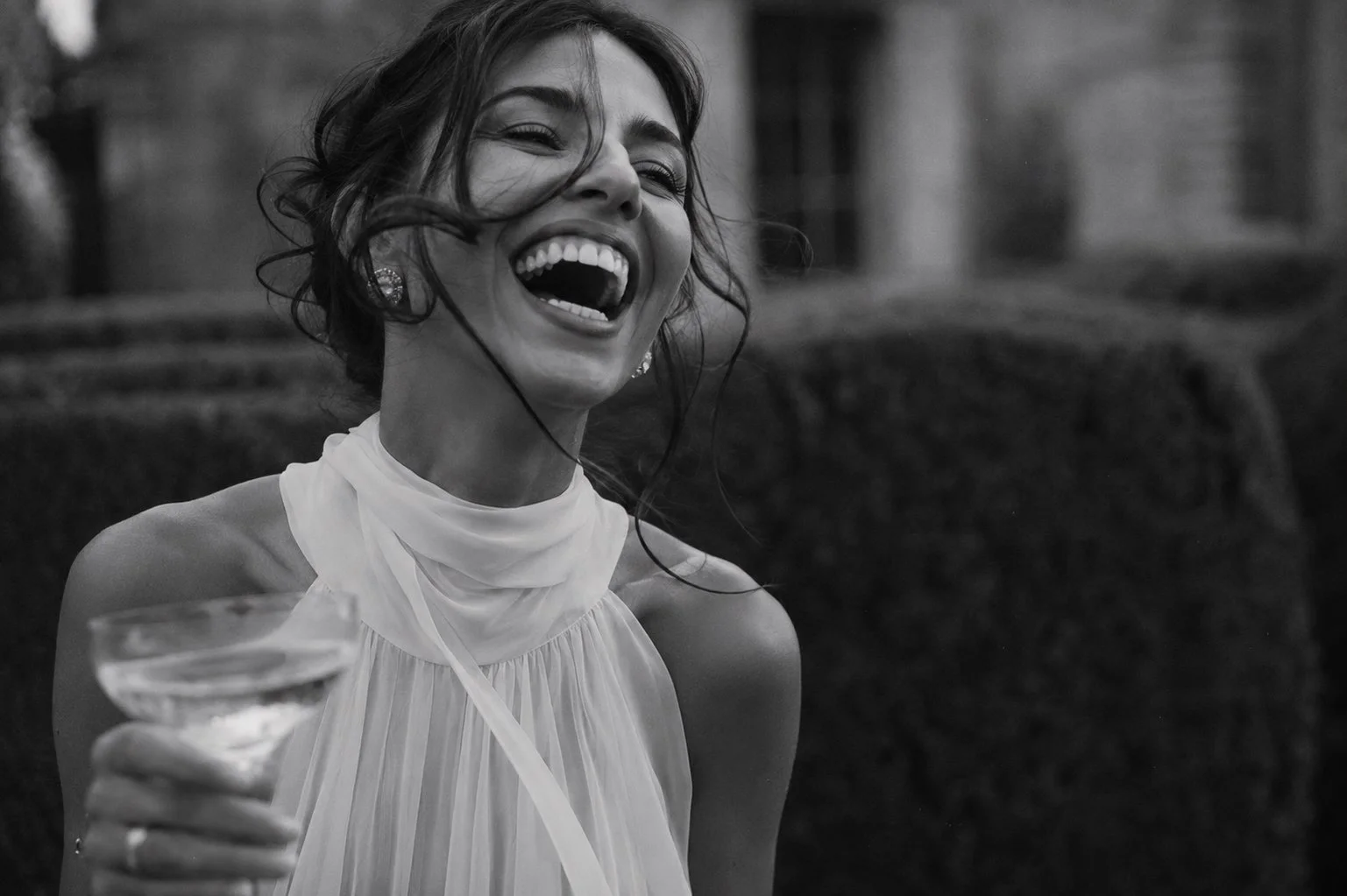 Bride laughing with a champagne coupe during a luxury château wedding in France, captured in timeless black and white.