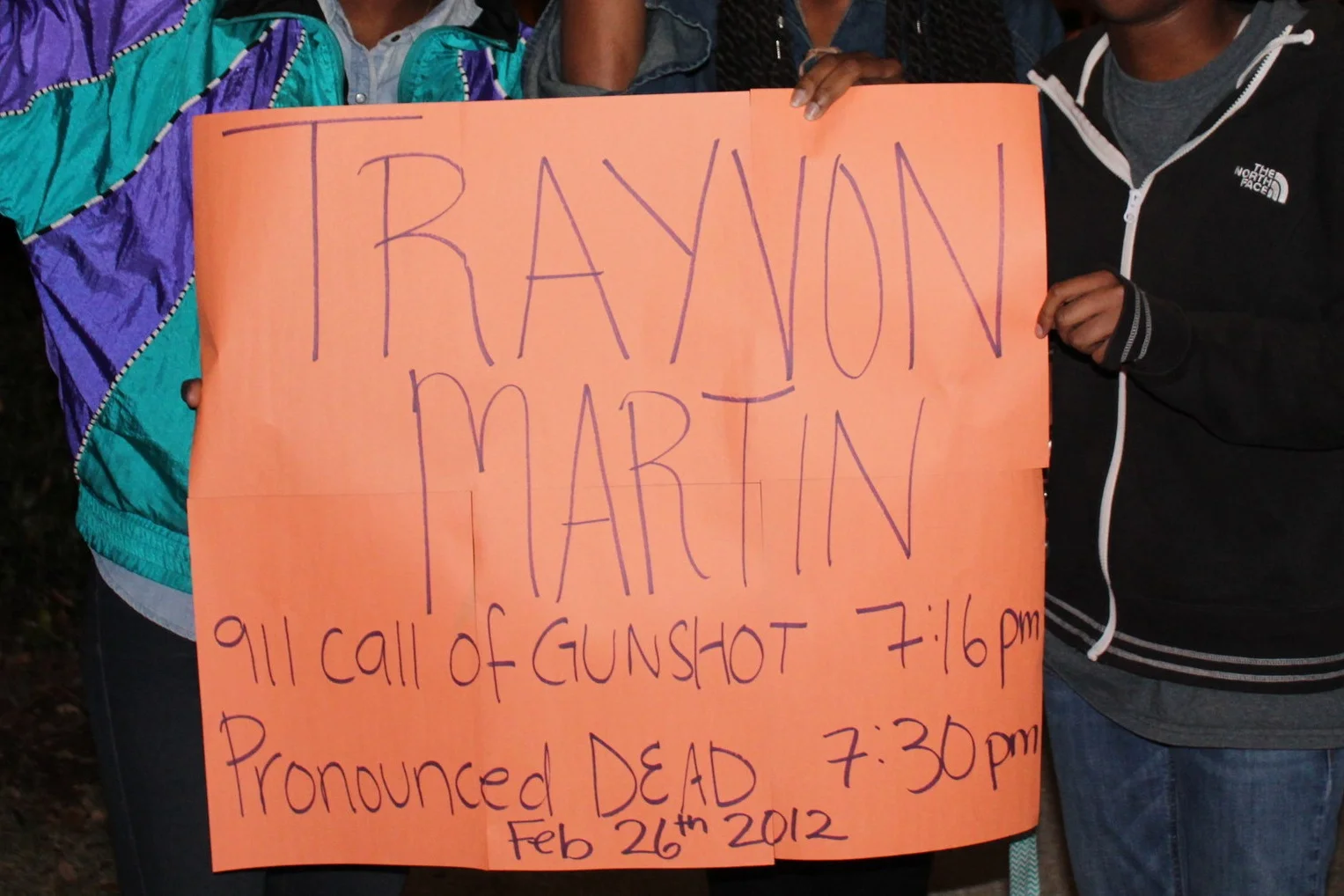 Becky Guerrier, Hasani Malone, and Kayla Lloyd hold up their sign that reads, “Trayvon Martin 911 call of gunshot 7:16 p.m. pronounced dead 7:30 p.m. Feb. 26 2012.”