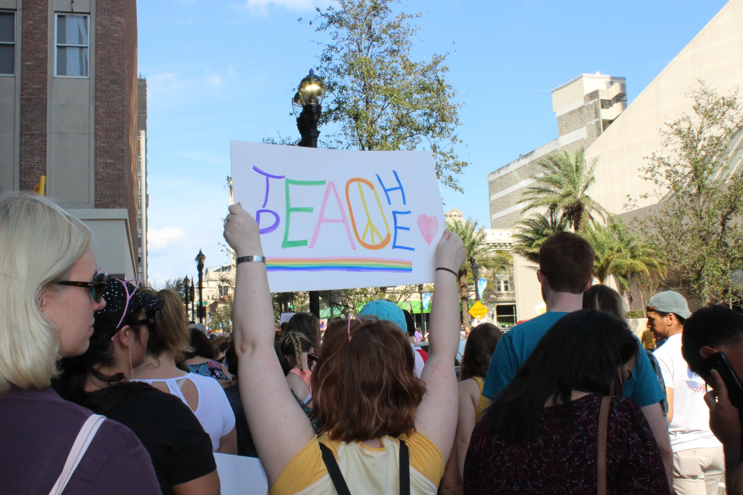 Young woman holds up a sign that reads “teach peace” at the Jacksonville Women’s March.