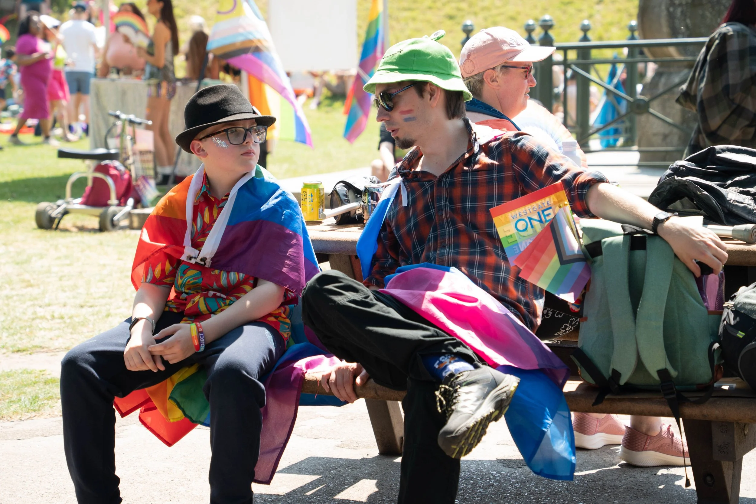 Photo of two people sat at a bench with LGBTQ+ flags.