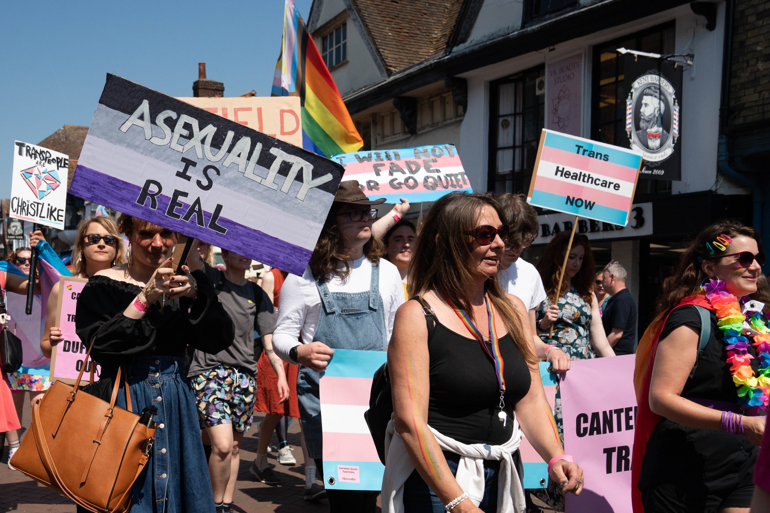 Photo of people in the Pride Canterbury Parade, including placards such as Asexuality is Real, and Trans Healthcare Now.