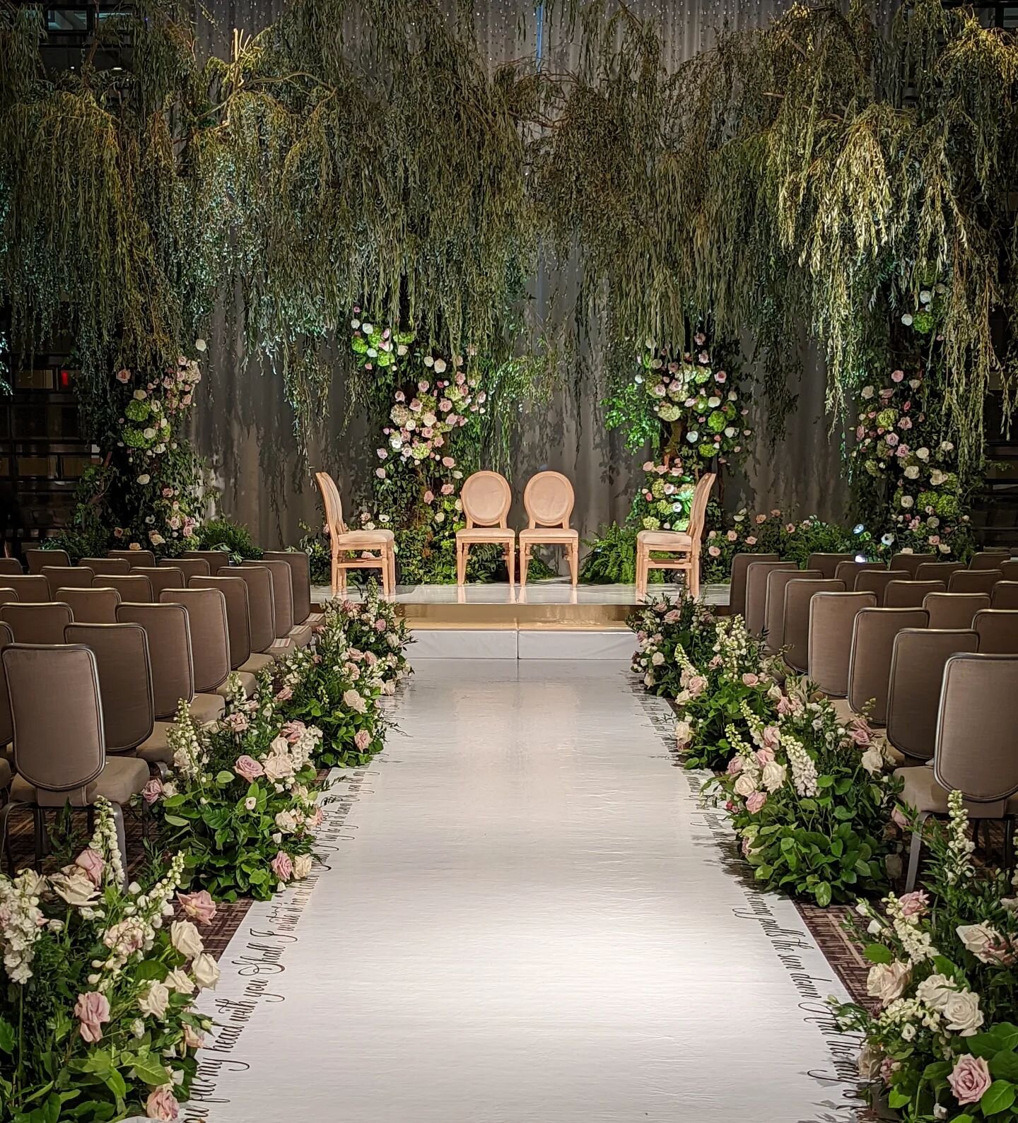 This morning's ceremony is a bountiful foliage display composed of towering willow trees augmented by climbing and trailing floral treatments. The trees envelop the couple in natural beauty. Designed in collaboration with the bride and masterfully pr