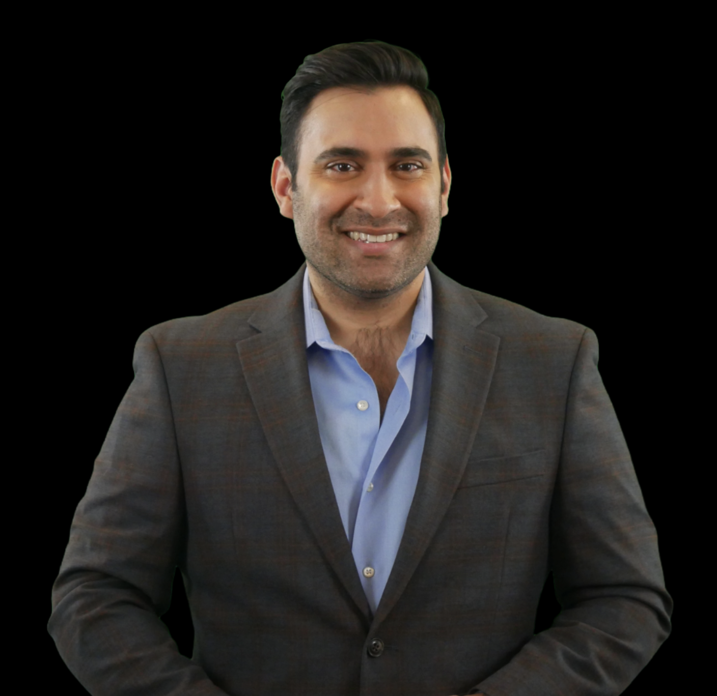 A smiling man in a gray suit jacket and blue shirt, sitting with hands folded, against a black background.