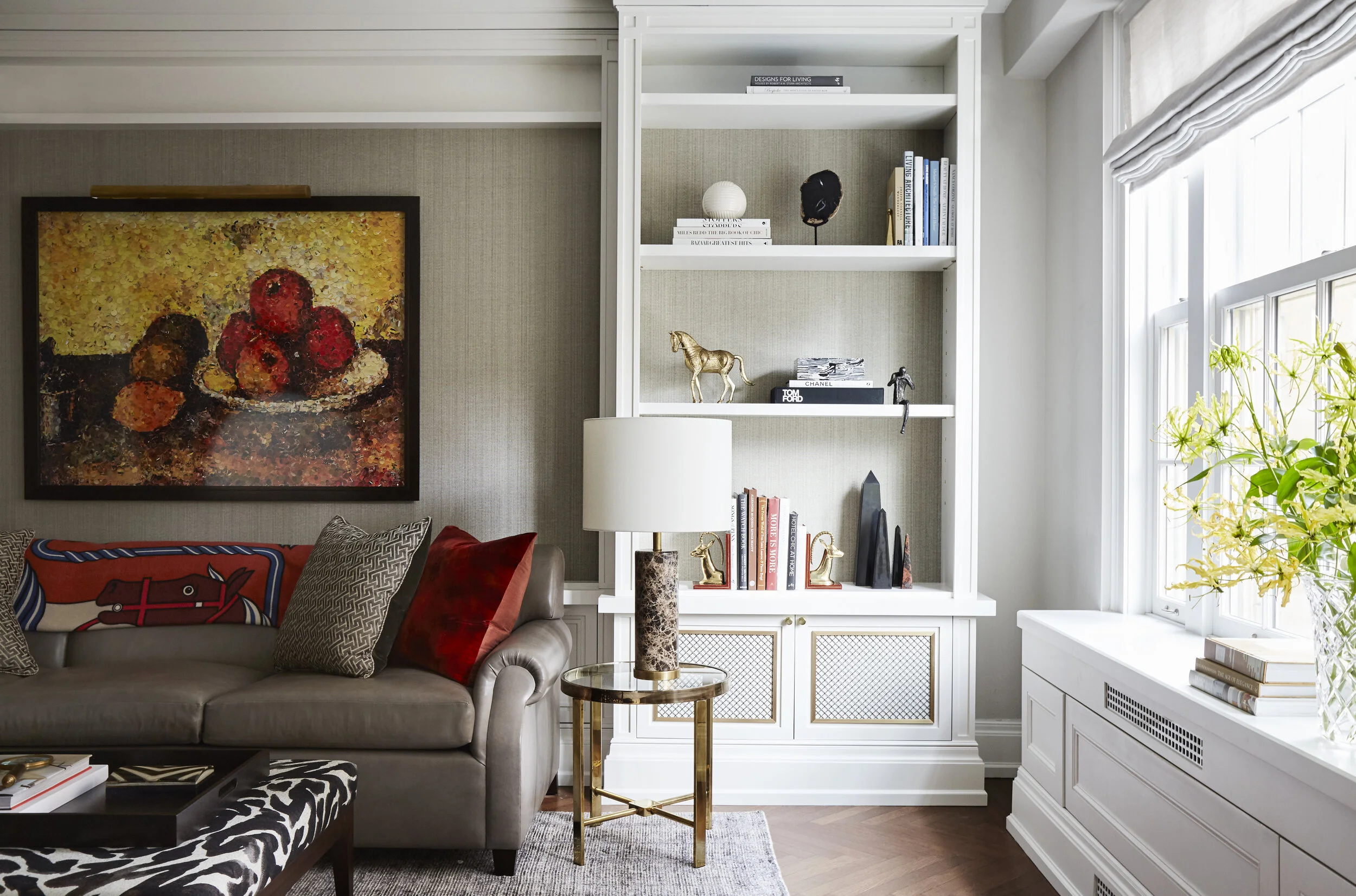 grasscloth walls with gray leather sofa, glass side table with large marble lamp and zebra print ottoman, with bookshelves