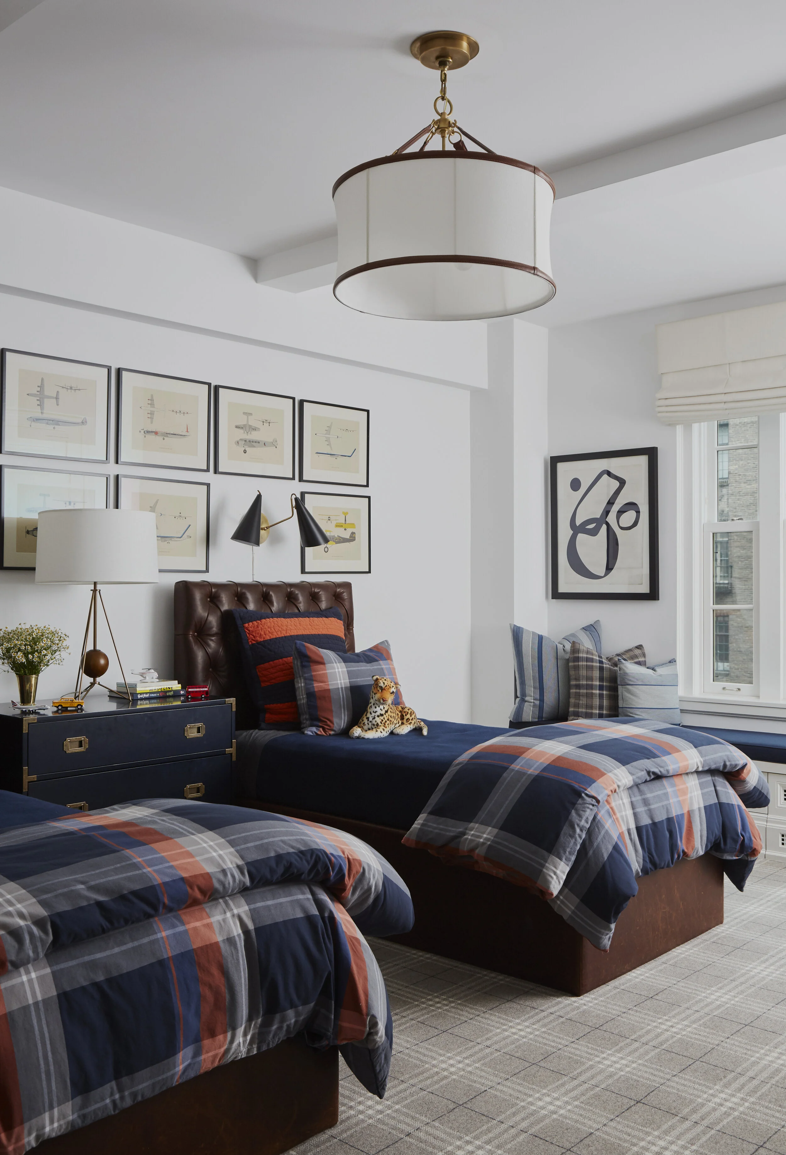 Twin leather beds with plaid blankets, navy blue dresser and artwork