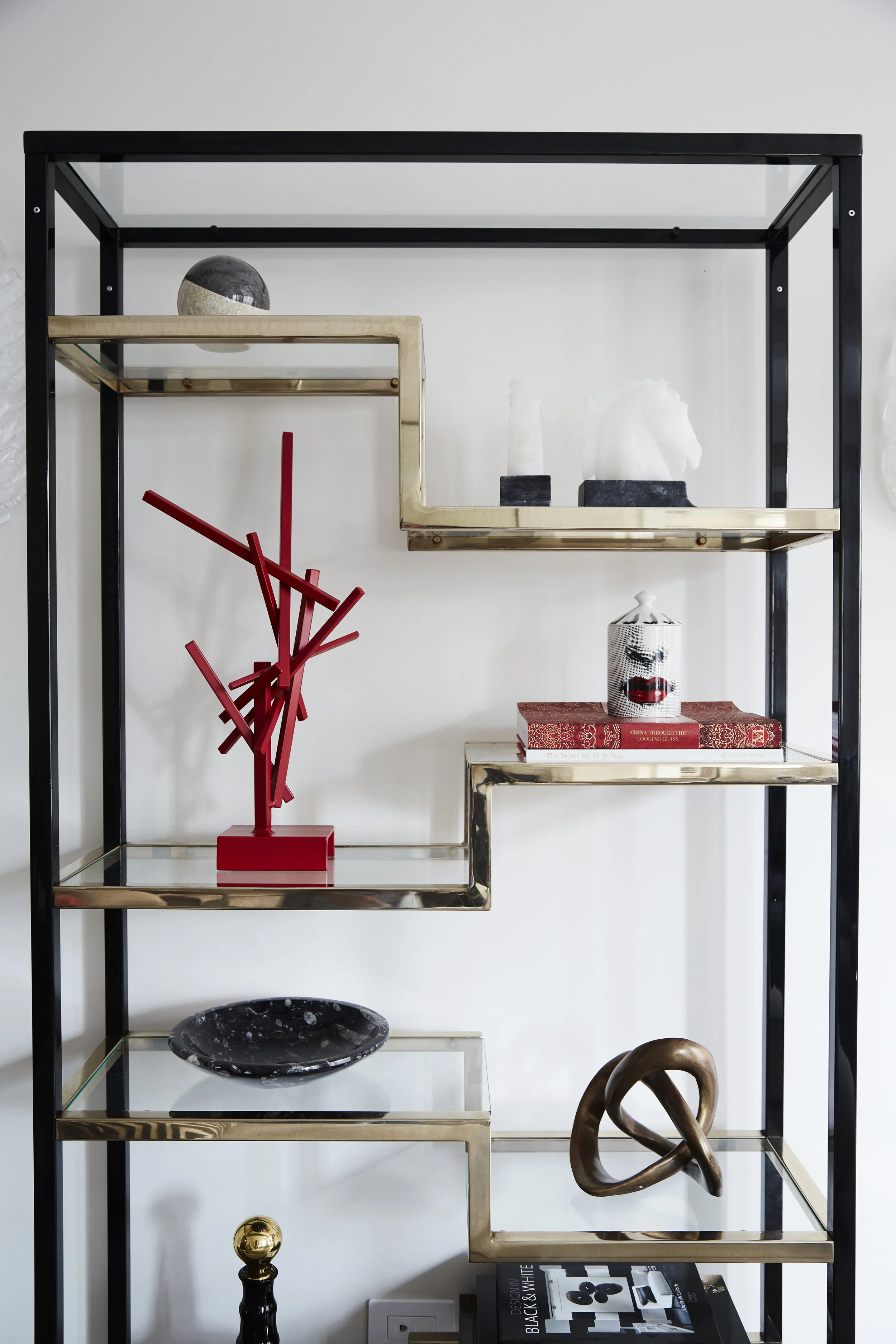 black and brass shelf with red accessories and sculptures