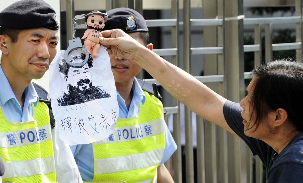   An activist holds a doll, a toy handcuff and a drawing of detained prominent Chinese artist Ai Weiwei in front of police officers during a protest to demand his release, in Hong Kong on April 24, 2011. Photo: Laurent Fievet/AFP.  