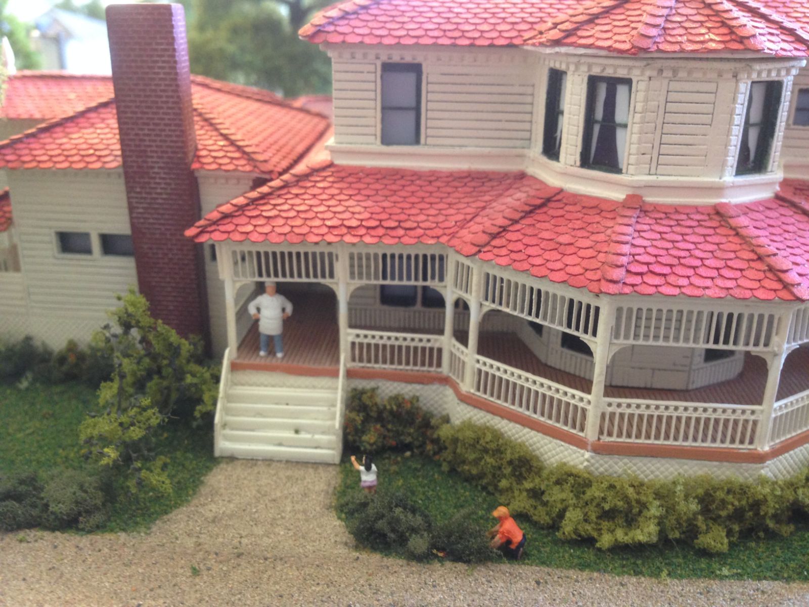 The house cook takes a break out on the porch while two of the children play hide and seek in the bushes.