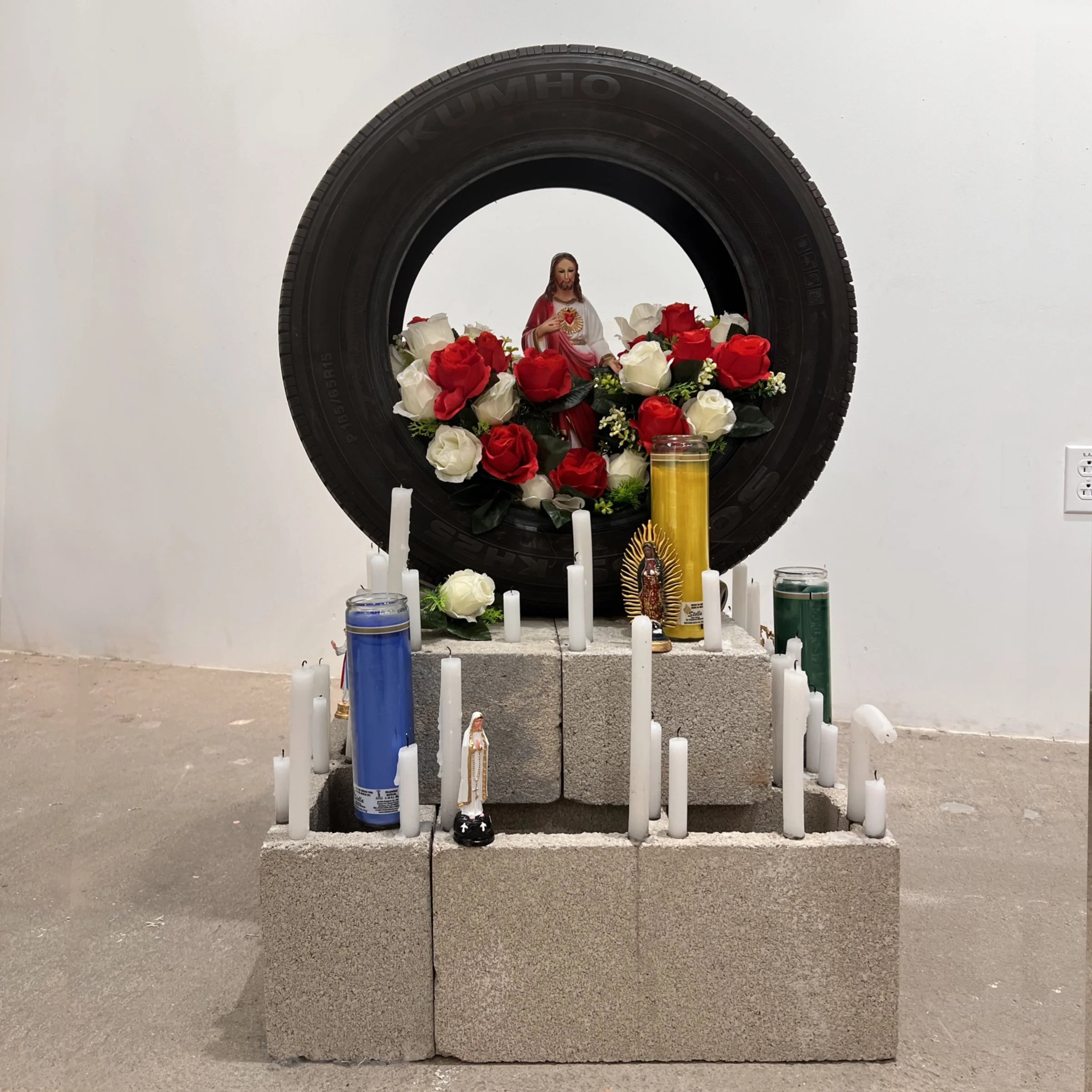 Tire as Reliquary (2025) Candlesticks, Cinder Blocks, Faux Florals, Saint Statues & Votive Candles as Assemblage Altar