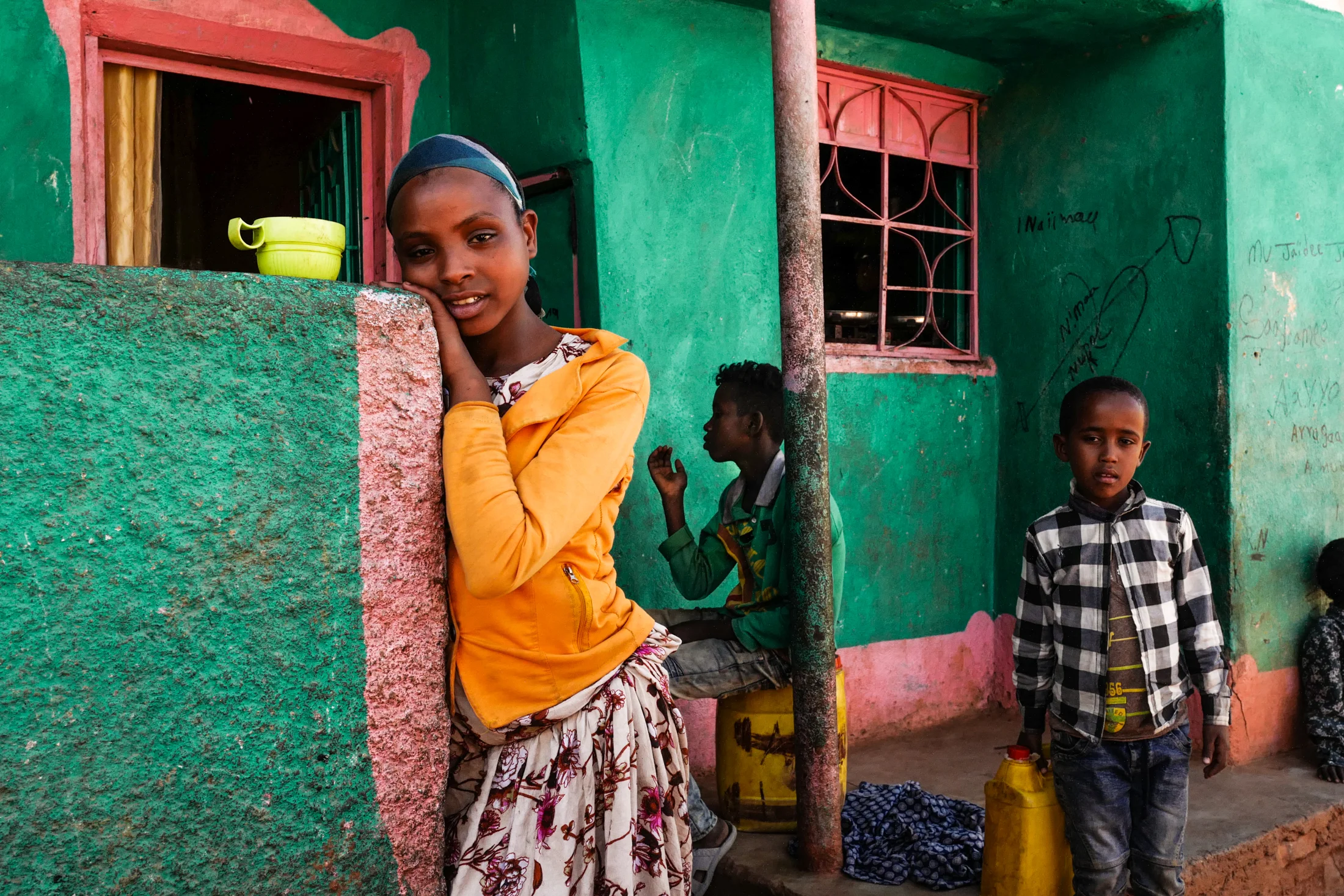 Children gathered in the porch of a shop. Two boys with yellow jugs are to collect drinking water.