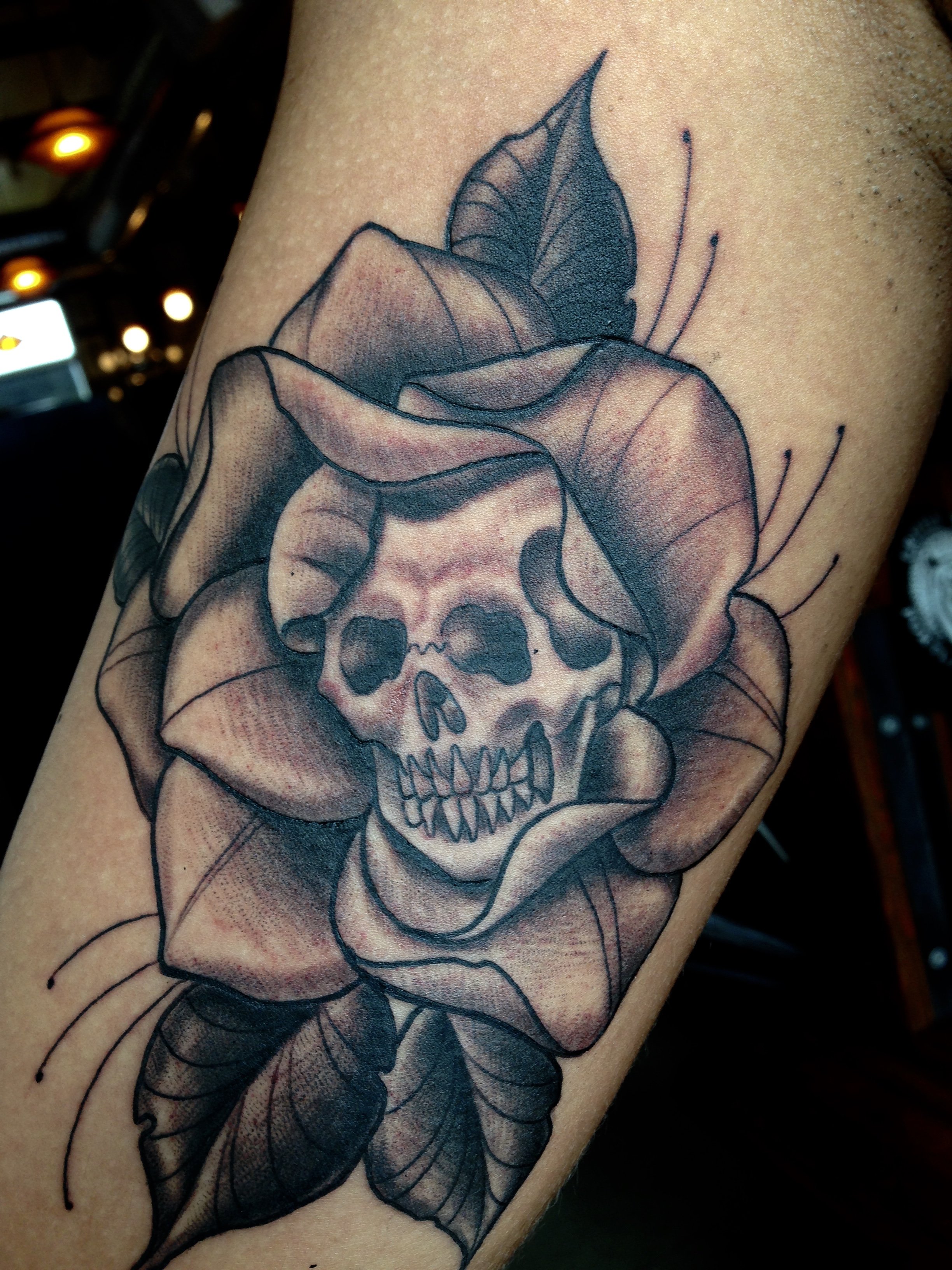 Tattoo of a skull surrounded by a large flower with several leaves.