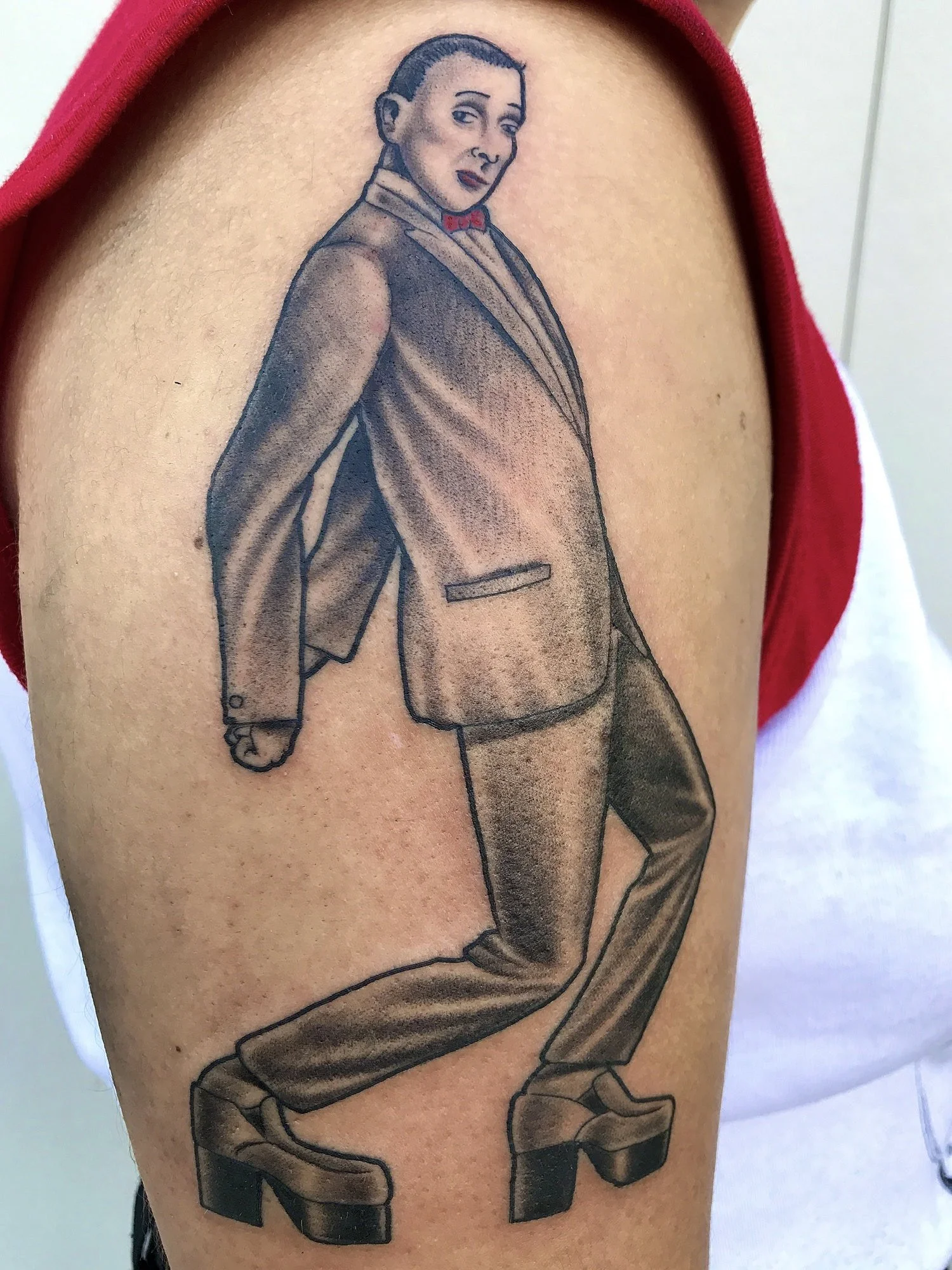 Tattoo of a Pee Wee Herman in formal attire, wearing large platform shoes, with a serious facial expression.