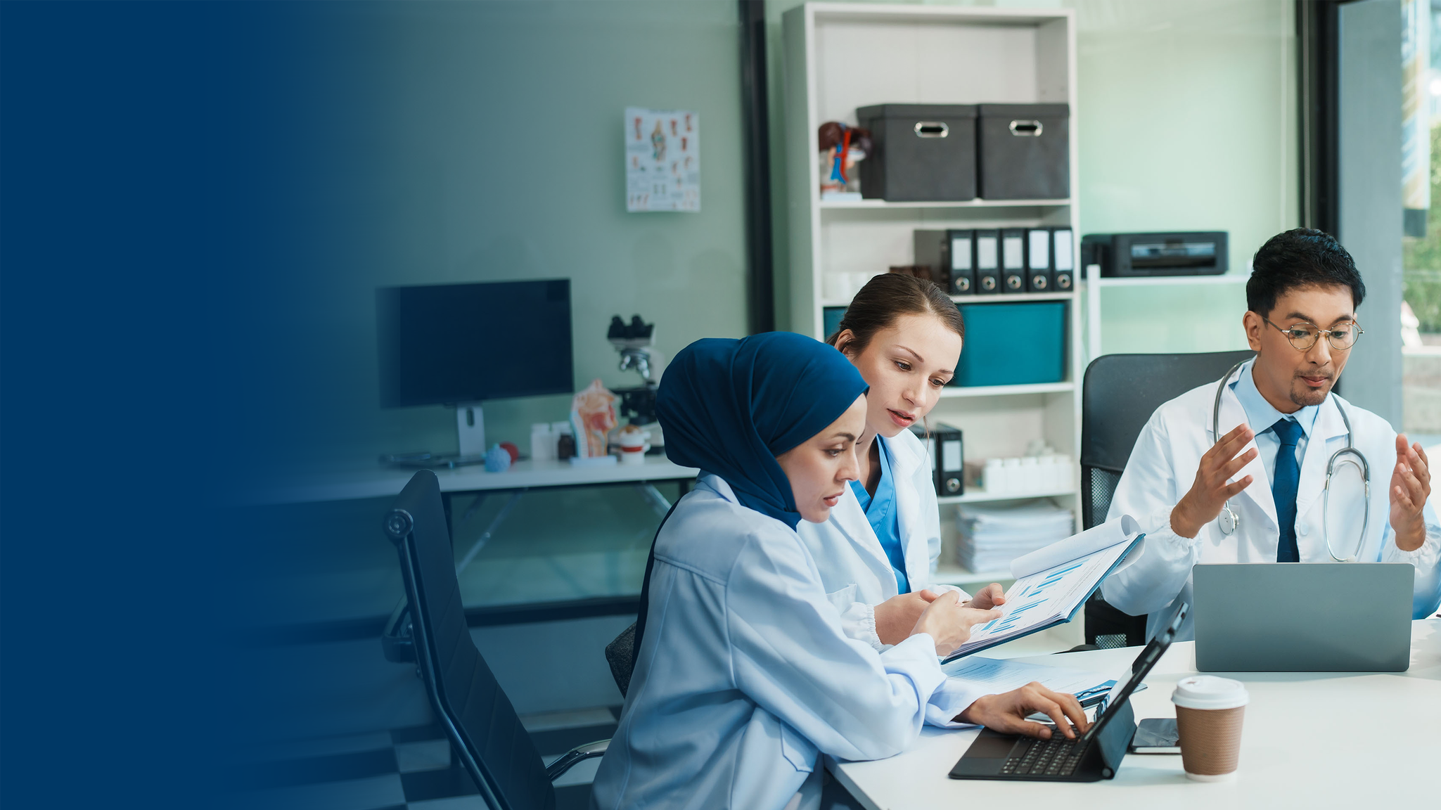 Group of three diverse healthcare professionals, including a woman wearing a hijab, working together in a medical office with medical supplies and office supplies in the background.