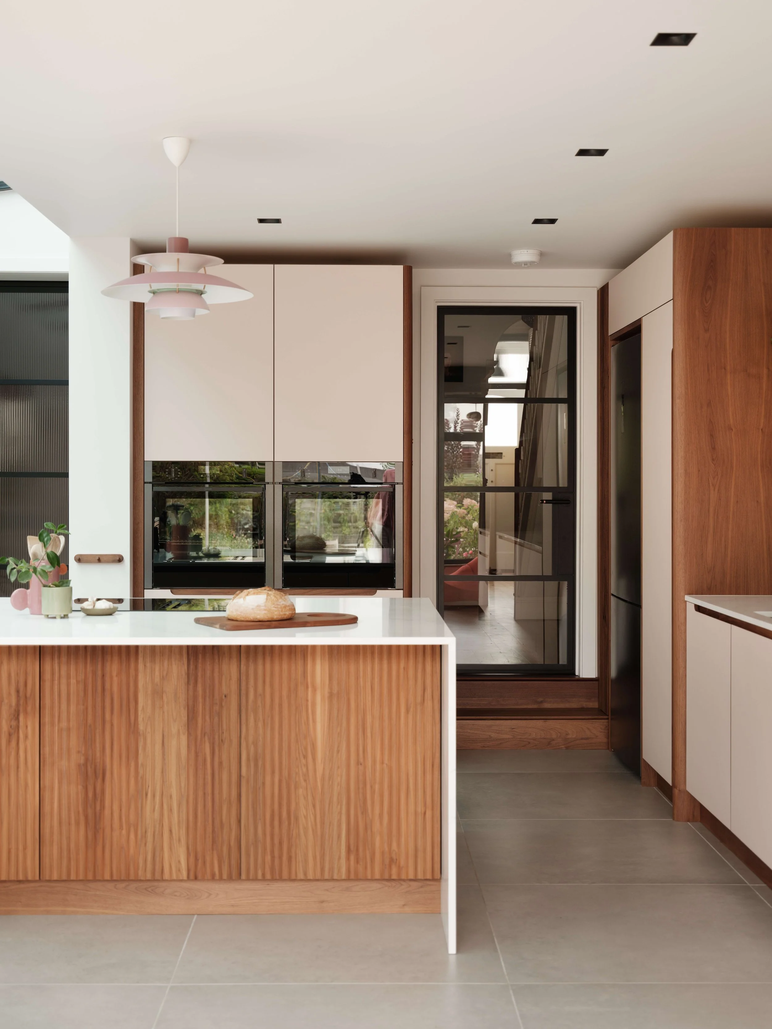 Modern kitchen with wooden cabinets, white island, and glass door leading outside. Decorative plant and bread on the island.