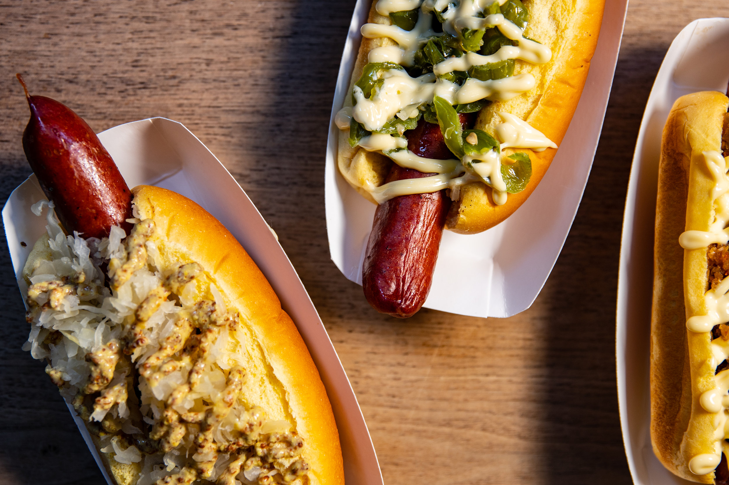 three hotdogs on a wood surface each covered in different toppings