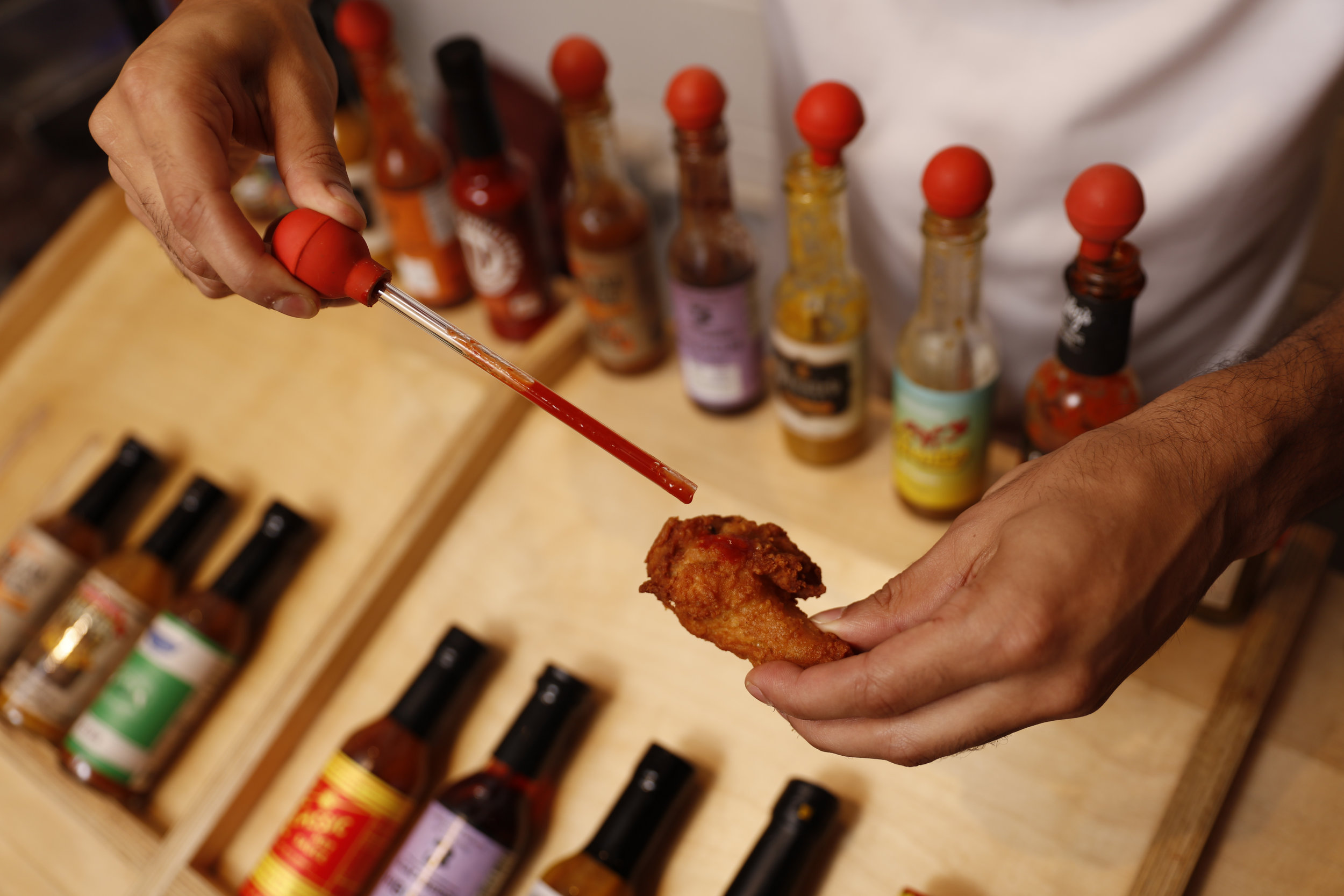 using dropper to drop hot sauce on a chicken wing