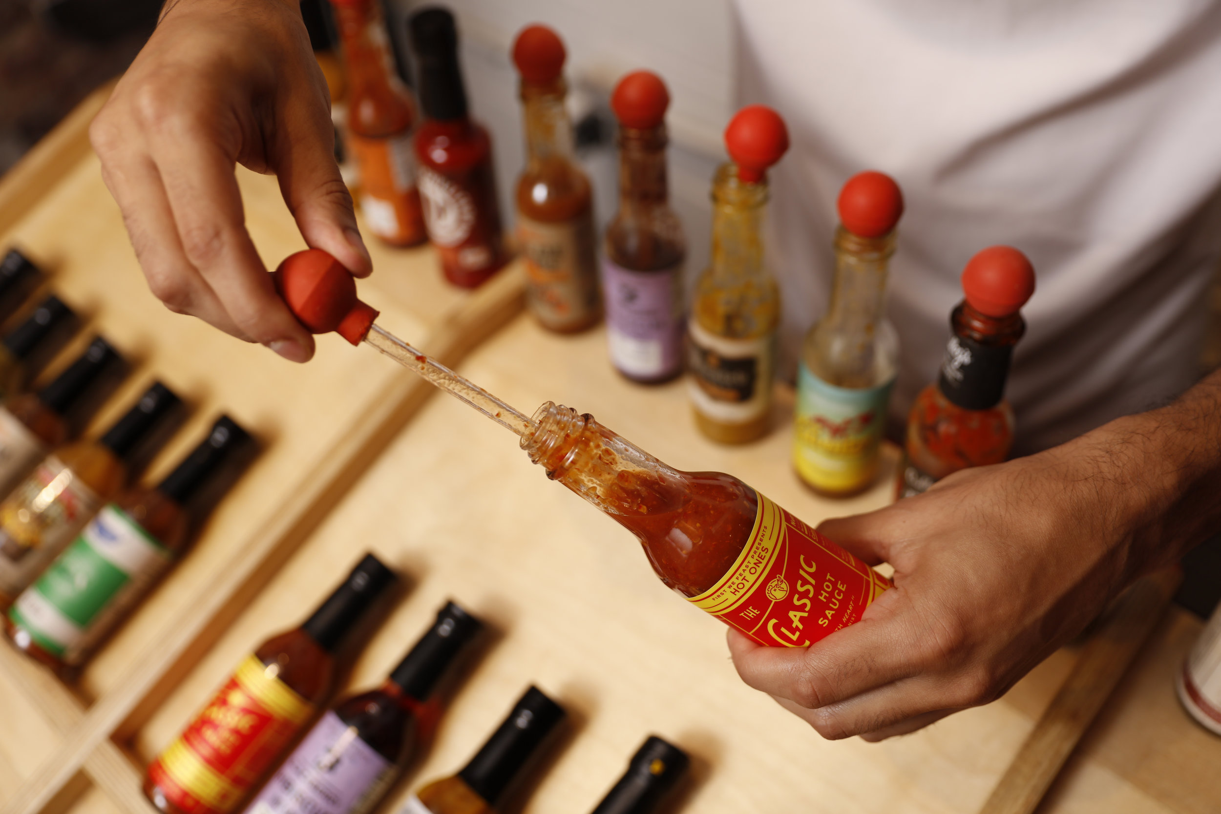 hand using a dropper to pull out a taste of hot sauce 