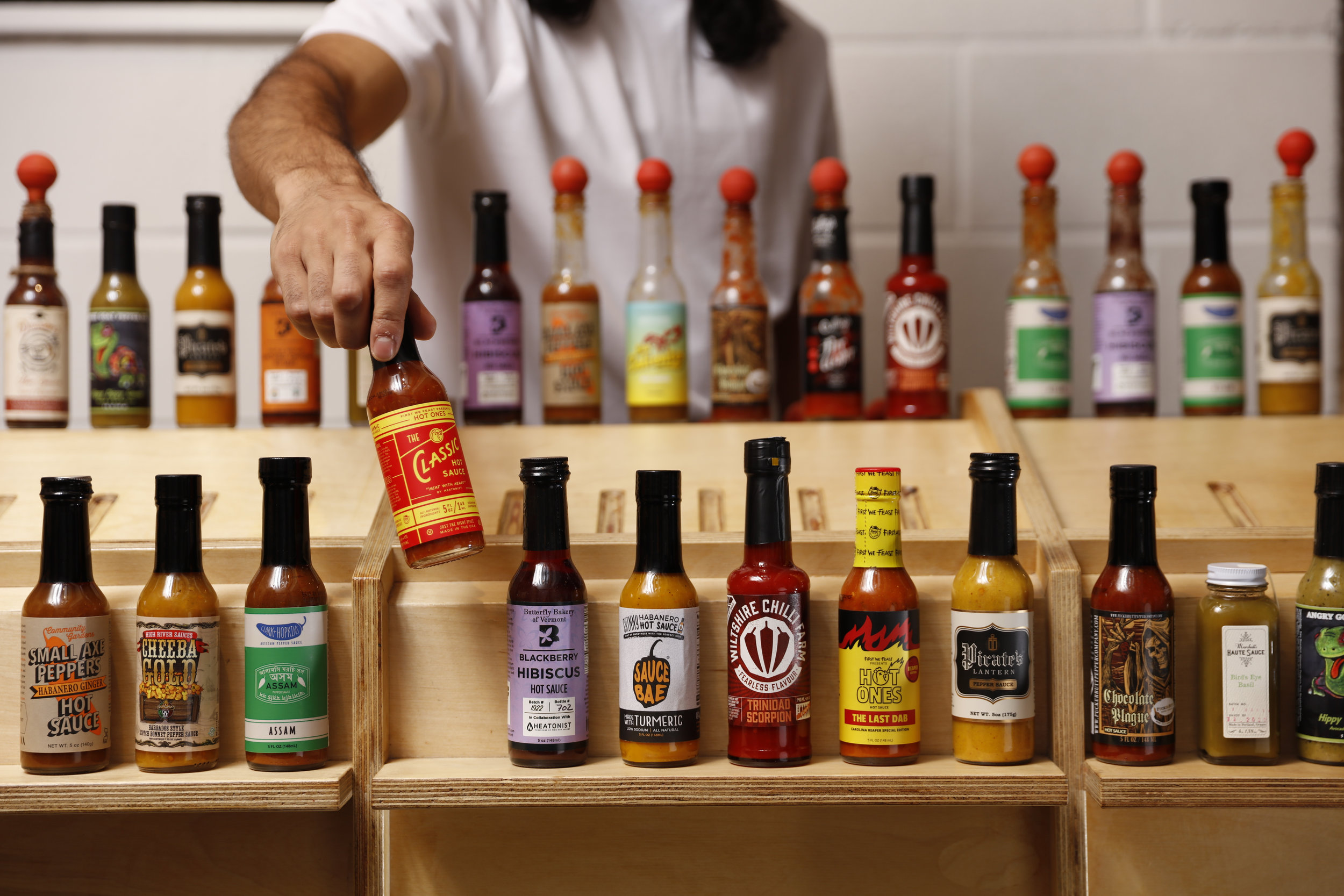 hand holding up one hot sauce bottles among many bottles of hot sauce 