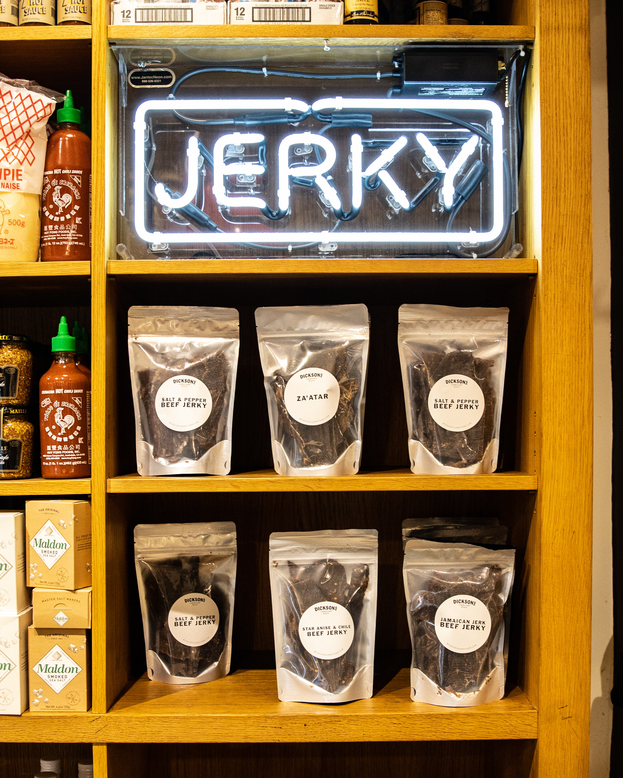 shelving with a neon sign reading Jerky with bags of jerky below it 
