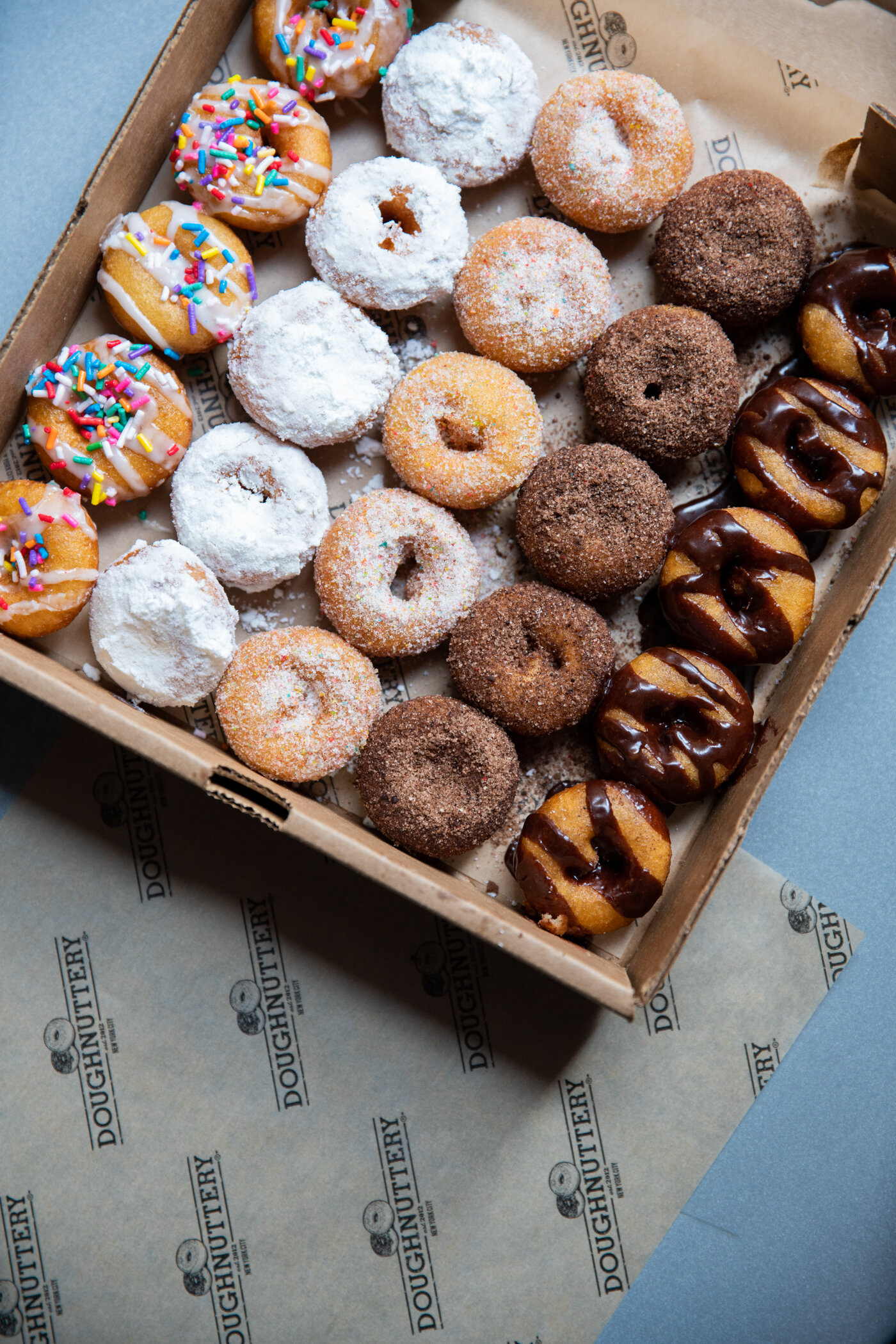 box of varying types of doughnuts, some with sprinkles, some with sugar, some with powder