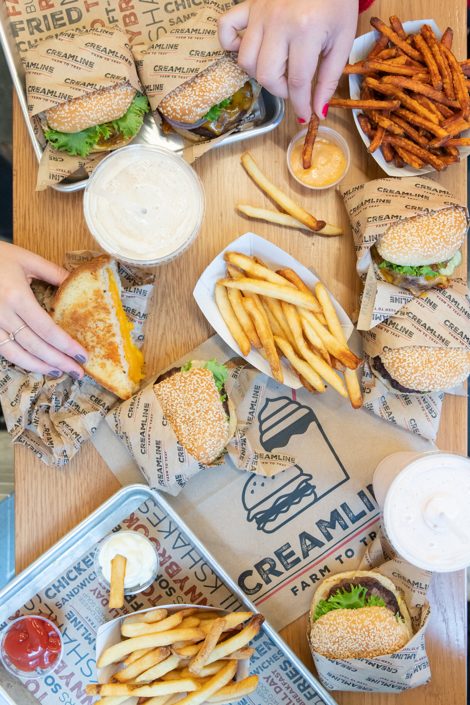 overhead shot of a hand grabbing half a sandwich with hamburgers and fries and milkshakes covering the table