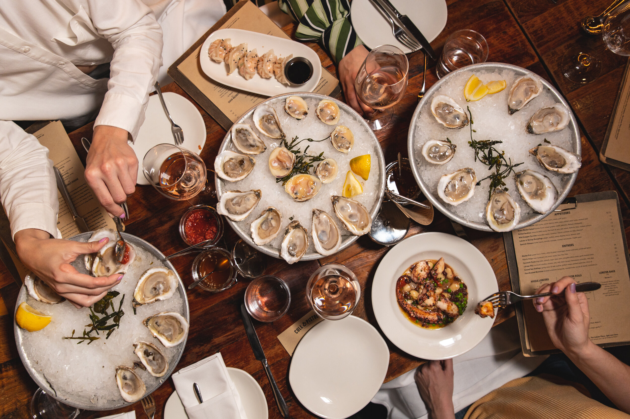 overhead shot of 3 trays of oysters and clams on the half shell with hands grabbing some