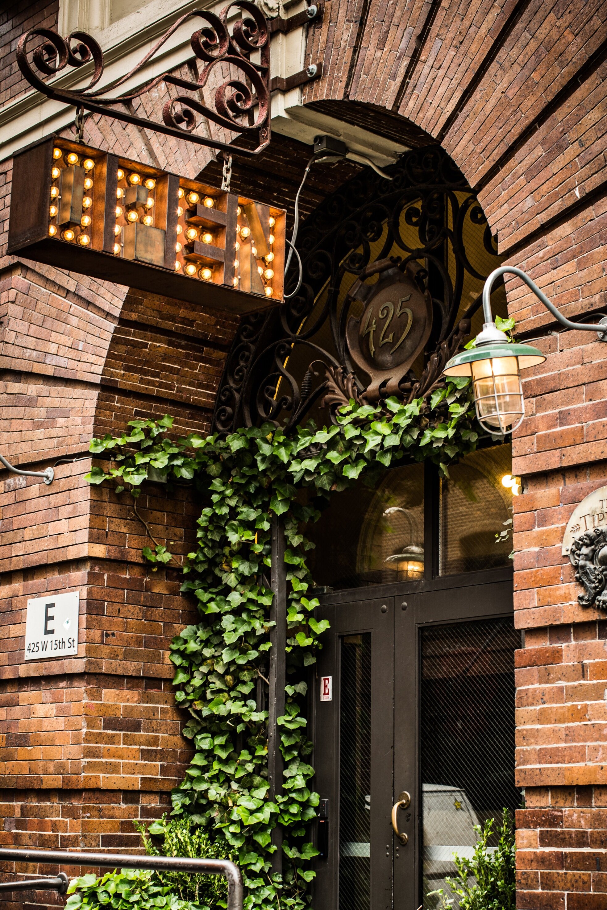 brick building with ivy growing up the side, metal sign hanging saying "open" in lights