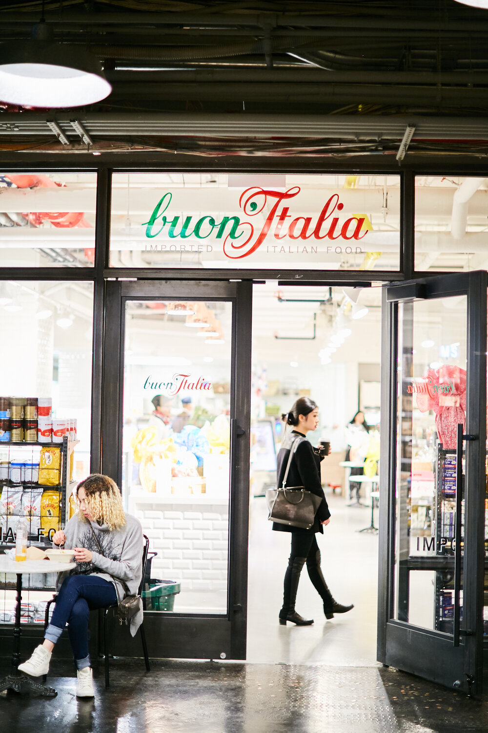 Buon Italia storefront with illuminated store in background with a customer walking in 