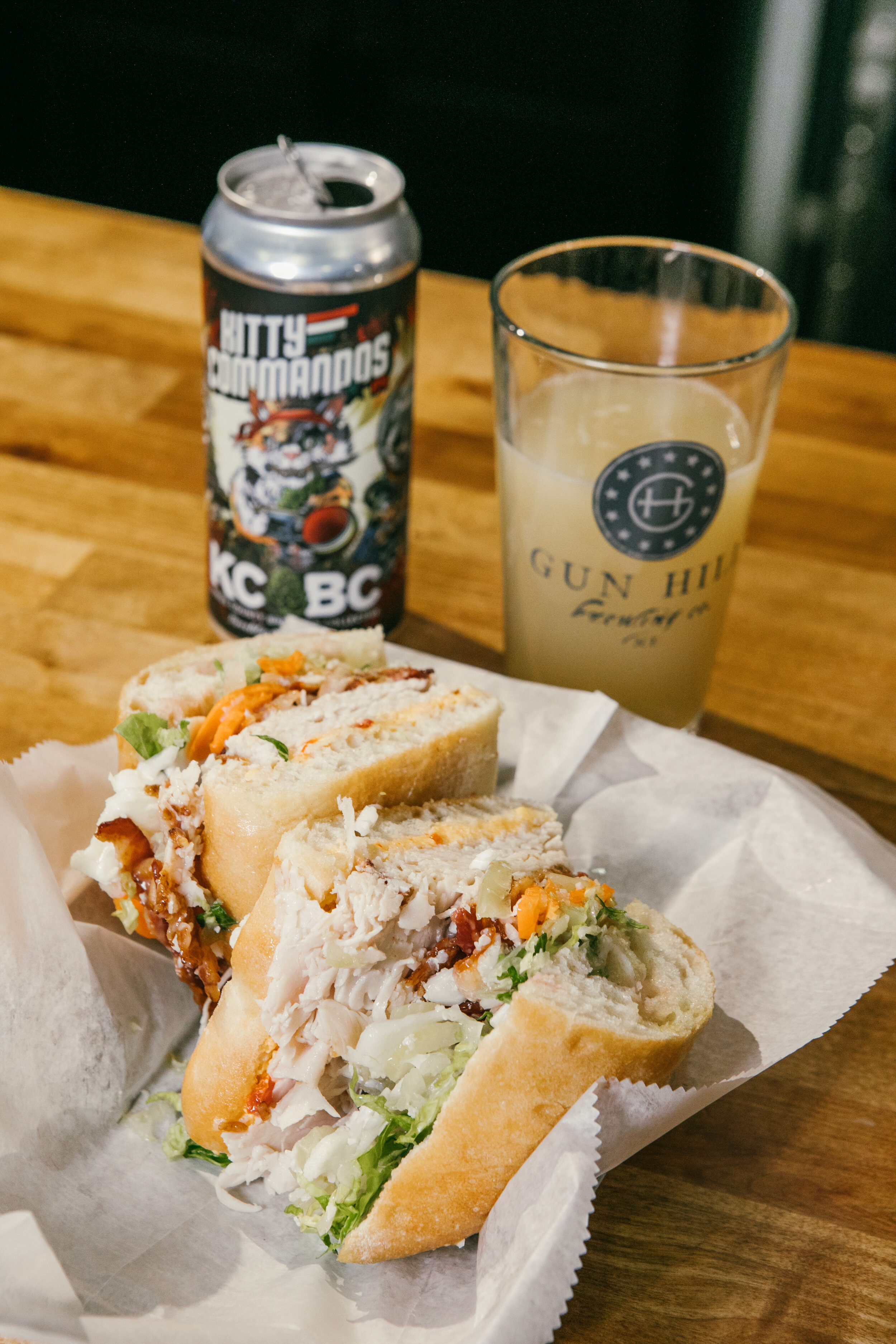 sandwich cut in half with a glass of beer and can in back ground 