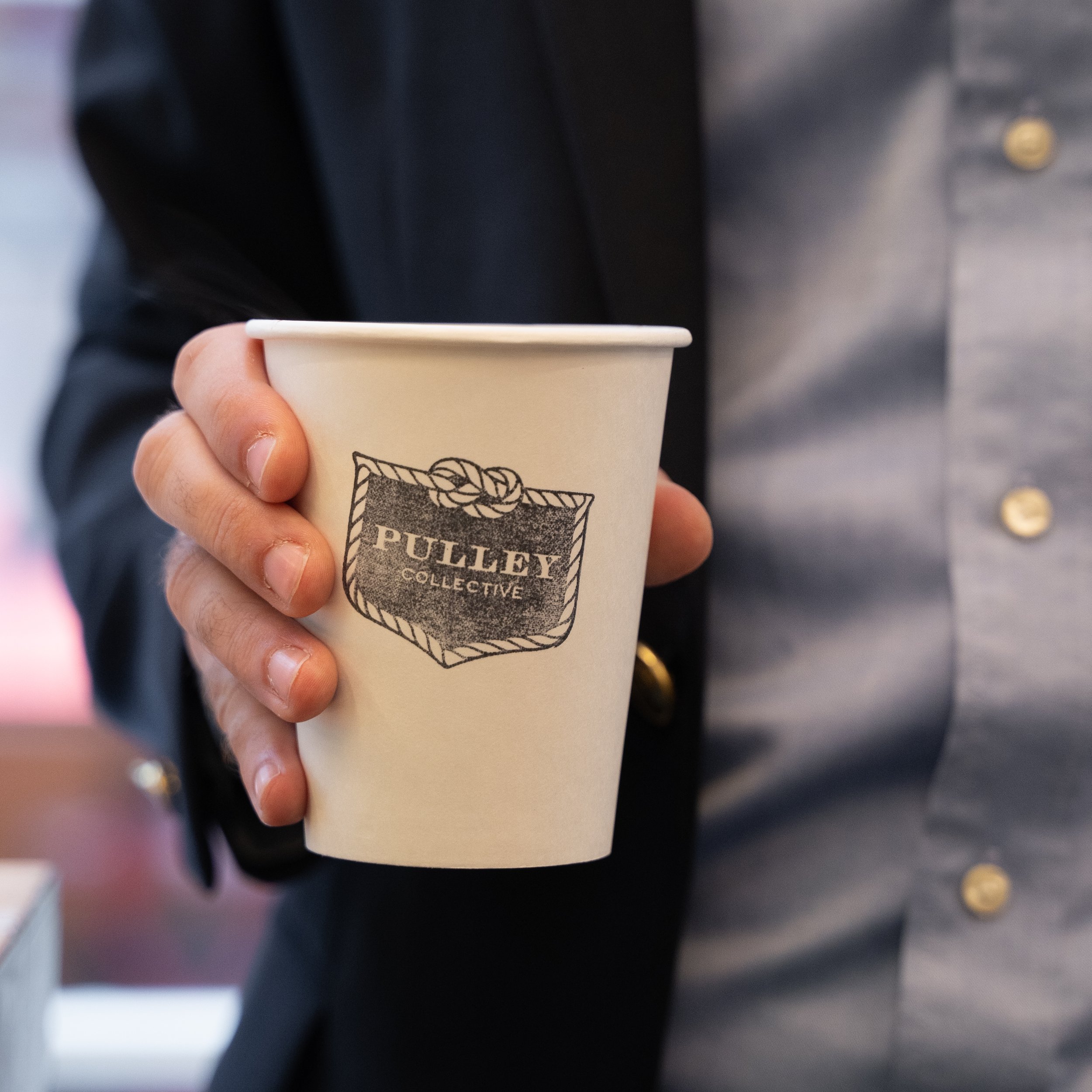 paper coffee cup with pulley collective brand held in a hand