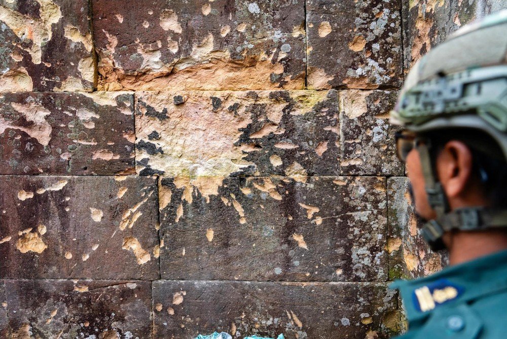 Cambodian military police officer looking at shell damage on the sandstone walls of Preah Vihear temple