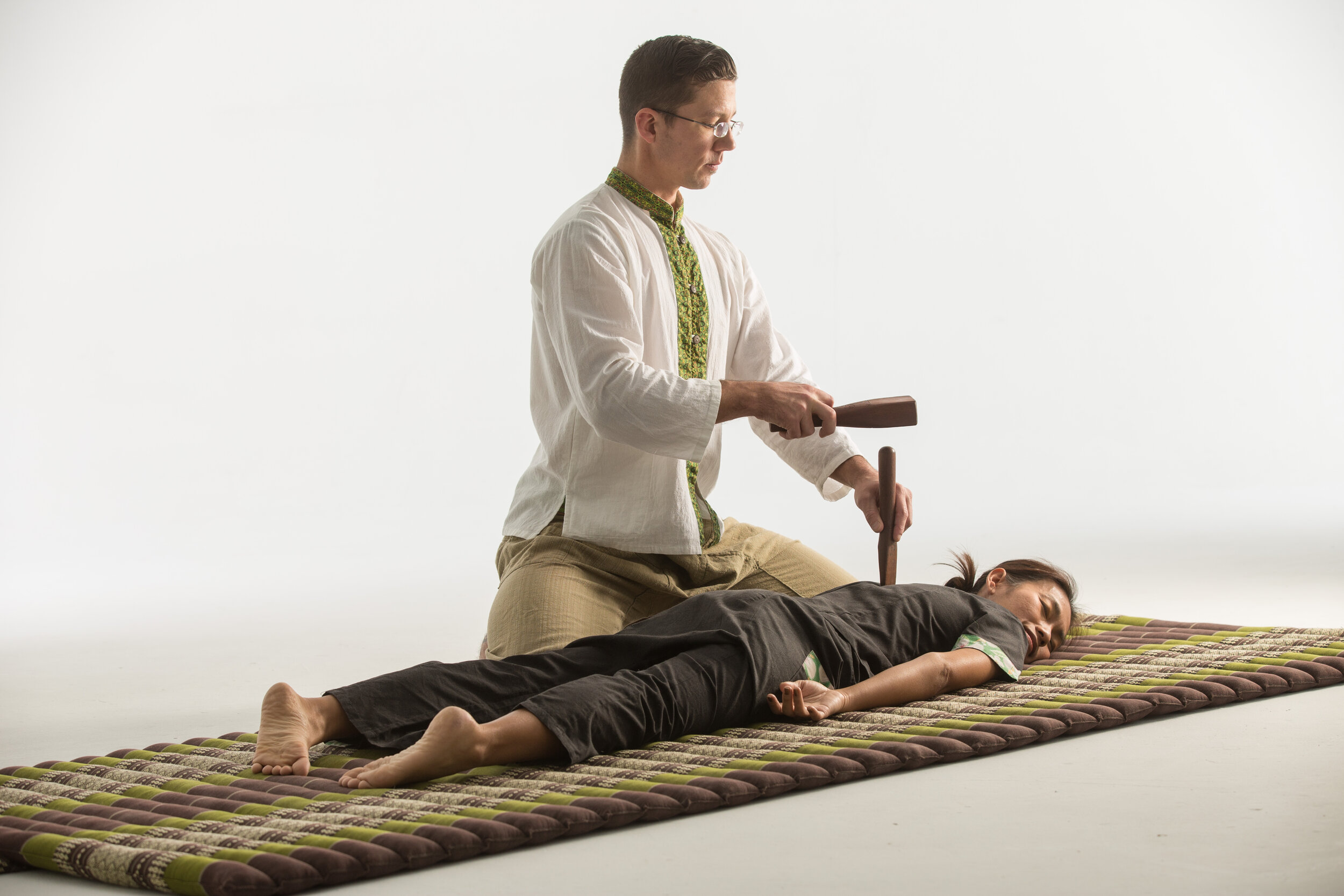 Kevin Lynch performing Tok Sen wooden tool therapy during a traditional Thai massage session