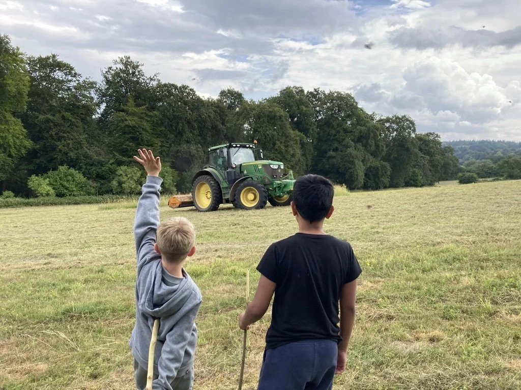 Two children waving at a tractor in a field