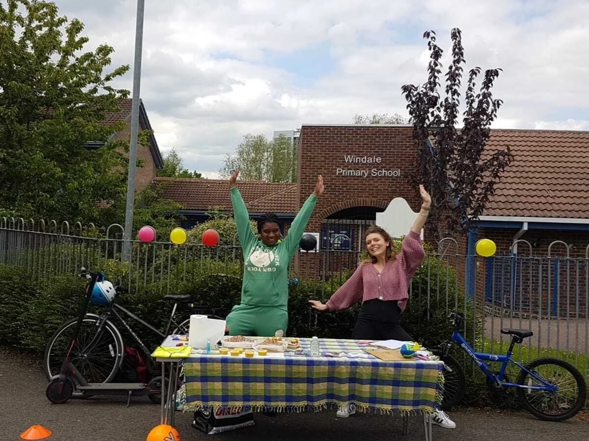 Two women, Oxford Hub staff members, posing at a stall outside Windale Primary School